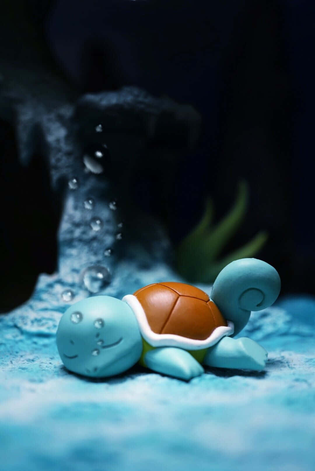 Pokemon Figures 桌布 壁紙 — 一個細小的藍色海龜雕像放置在帶有紋理的藍色表面上，背後有氣泡在黑暗的水下場景中升起。
