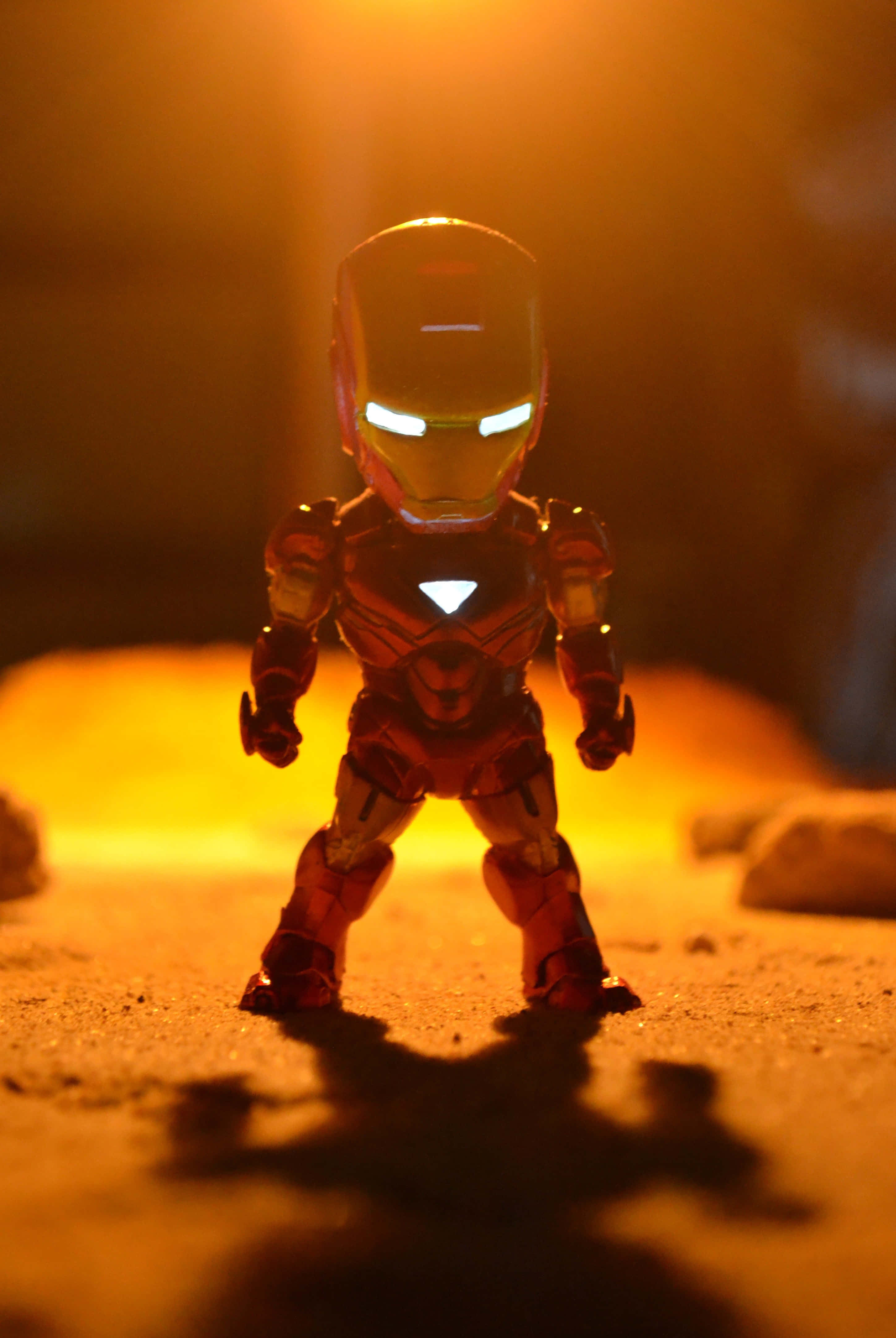 Iron Man Action Figures 桌布 壁紙 — 一個細小的鐵甲奇俠動作人偶在溫暖的金色光線照射下，在紋理地面上投下清晰的陰影。