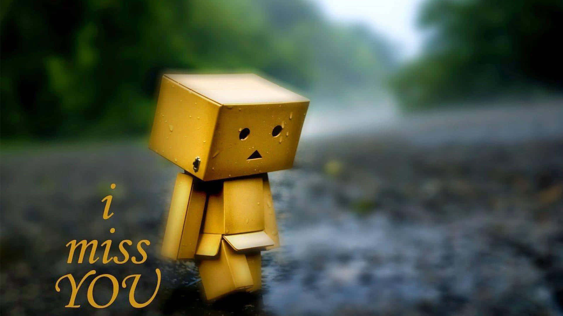 I Miss You 桌布 壁紙 — 一個細小的黃色紙箱角色獨自站在雨中潮濕的小路上，背景是模糊的綠色森林。