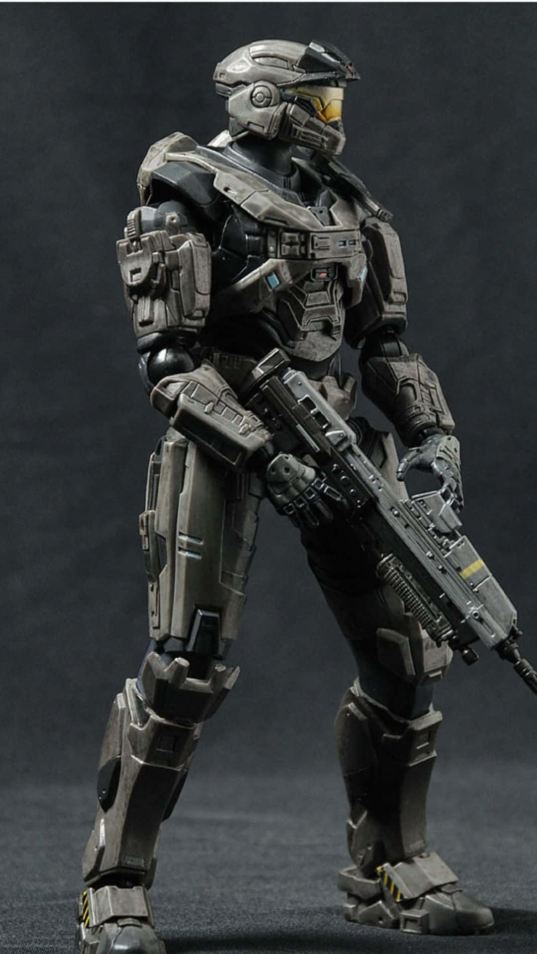 Noble Six 桌布 壁紙 — 一個細節豐富的灰色裝甲士兵人偶，在黑暗的攝影棚背景下，手持未來主義步槍，擺出準備姿勢。