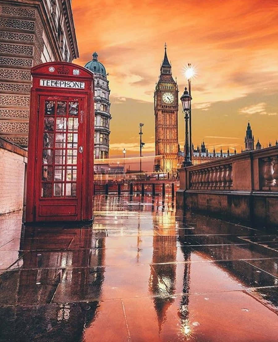 England 桌布 壁紙 — 一個經典的紅色電話亭矗立在潮濕的倫敦街道上，夕陽映照著大笨鐘和金色的天空。