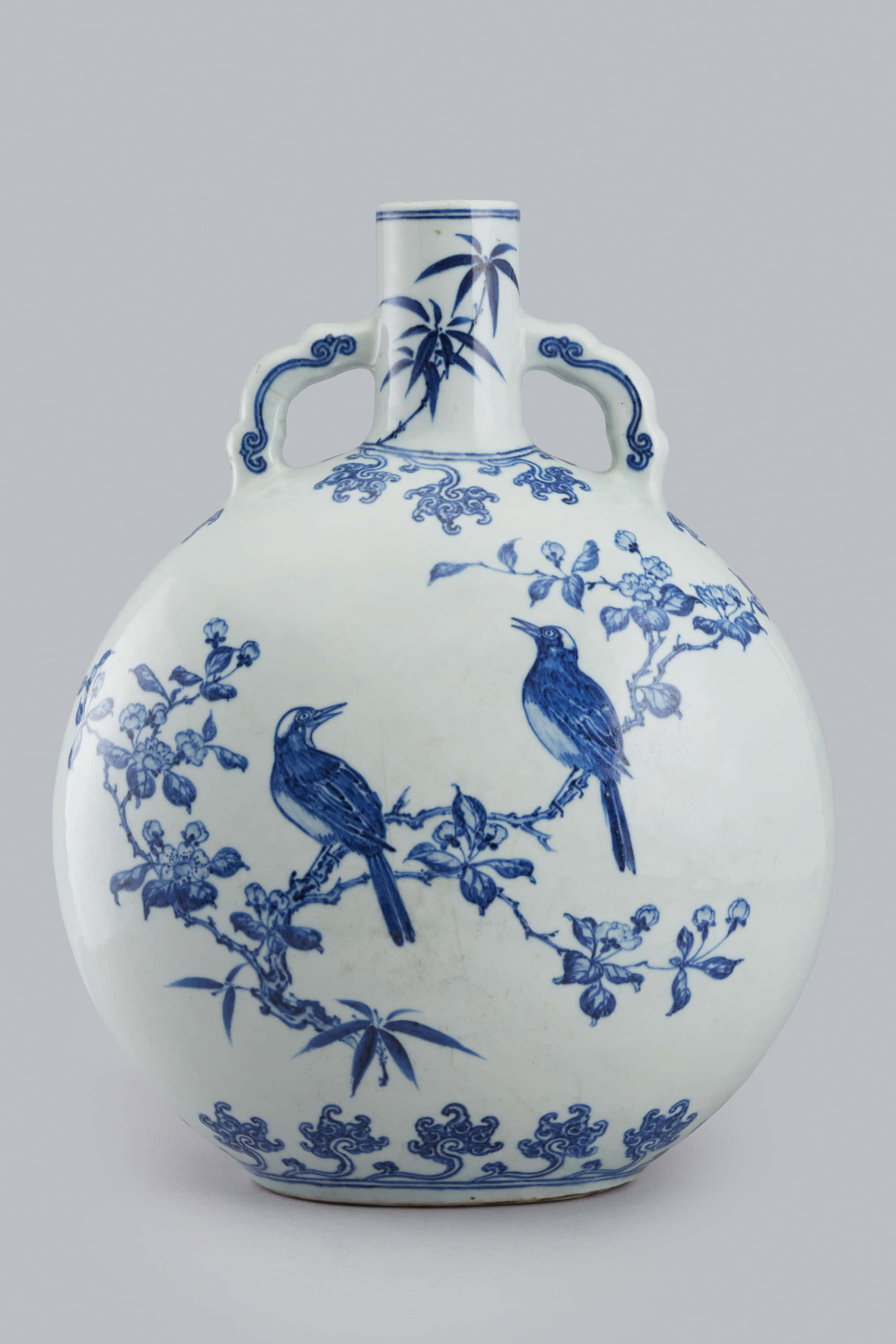 Ceramic 桌布 壁紙 — 一個經典的藍白瓷花瓶，有兩個手柄，上面有精緻的手繪鳥兒棲息在開花的樹枝上。
