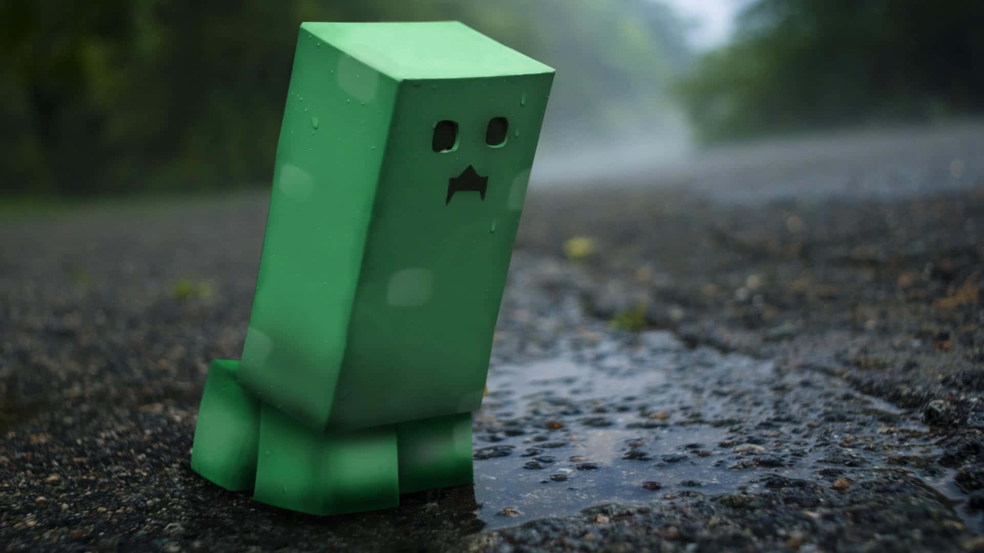 型格 Minecraft 桌布 壁紙 — 一個綠色Minecraft爬行者在霧雨暴風中獨自站在濕漉漉的瀝青路上，背景是模糊的森林。