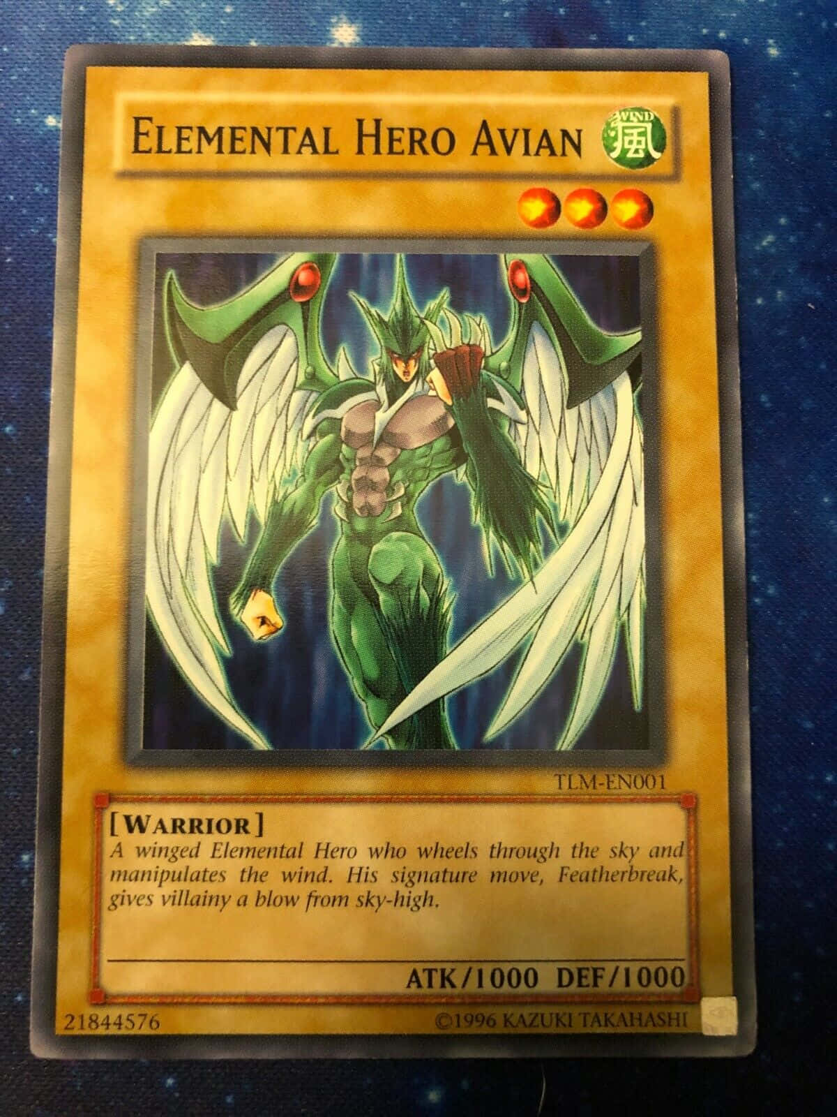 Yugioh Elemental Hero 桌布 壁紙 — 一個綠色有翼戰士，紅眼睛，白色羽毛翅膀，在Yu-Gi-Oh! 遊戲卡上，以深藍色星空為背景，蓄勢待發。