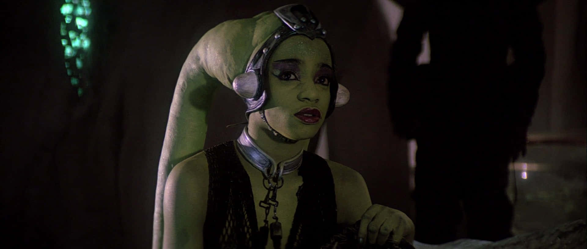 Twi'lek 桌布 壁紙 — 一個綠色皮膚、長頸、戴頭飾的外星女人，在昏暗的房間裡，帶著發光的綠色點綴，凝視前方。