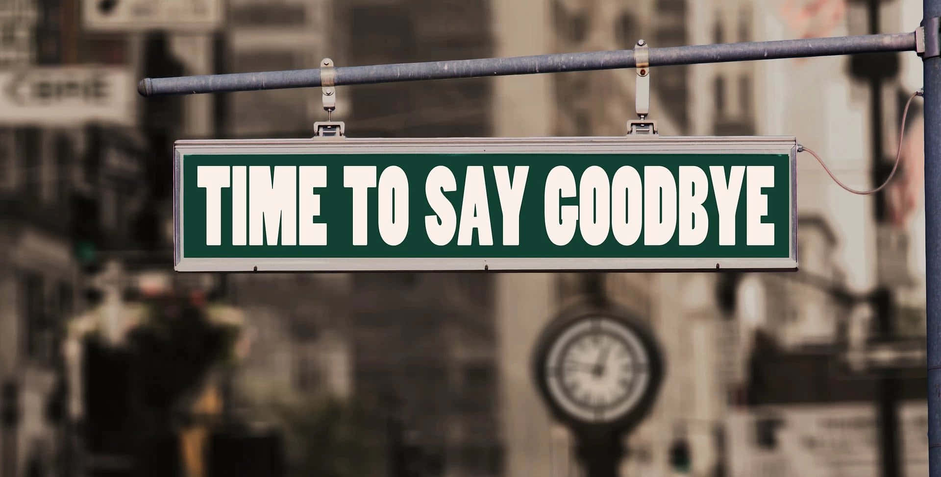 再見 桌布 壁紙 — 一個綠色路牌寫著「TIME TO SAY GOODBYE」，懸掛在模糊的城市街道上方，背景可見一個時鐘。