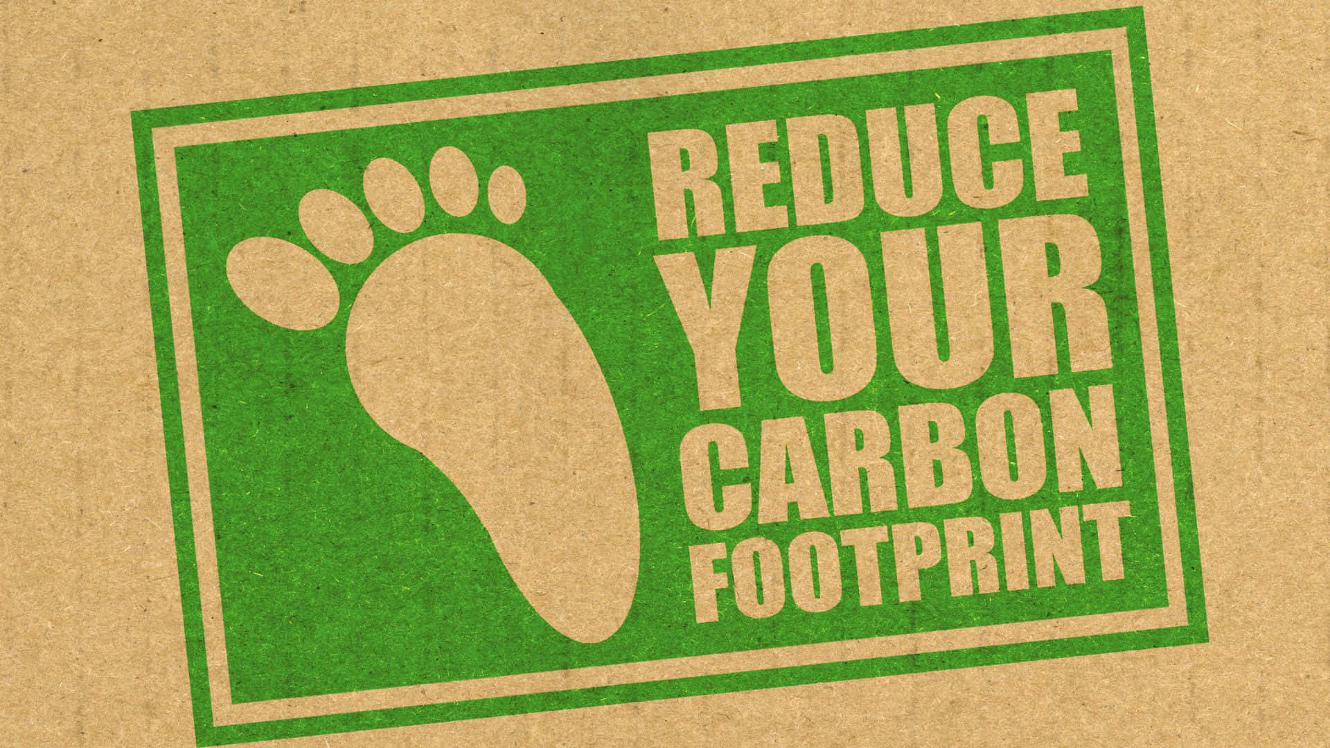 Carbon Footprint 桌布 壁紙 — 一個綠色長方形環保貼紙貼在棕色牛皮紙上，用腳印圖標敦促觀眾減少碳足跡。