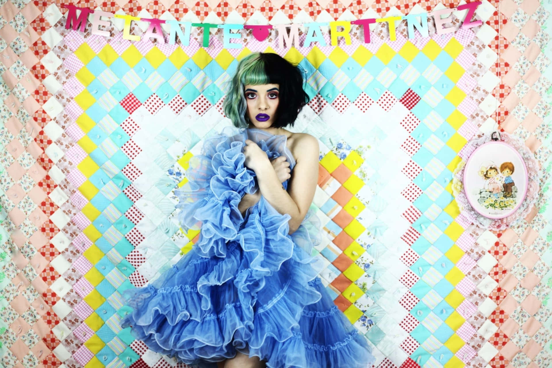 Melanie Martinez 桌布 壁紙 — 一個綠髮紫唇的人穿著一件寬大的藍色荷葉邊連衣裙，背景是色彩繽紛的拼布被子。