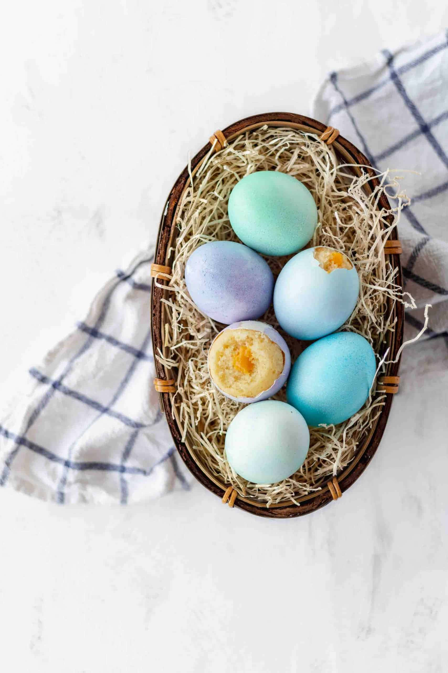 Eggshell 桌布 壁紙 — 一個編織籃子裝滿粉藍色和綠色復活蛋，有些裂開露出蛋黃，放在格仔布上的稻草上。