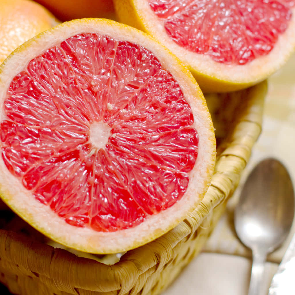 Pink Grapefruit 桌布 壁紙 — 一個編織籃子裡有鮮紅色西柚半邊的特寫，旁邊放著一個勺子。