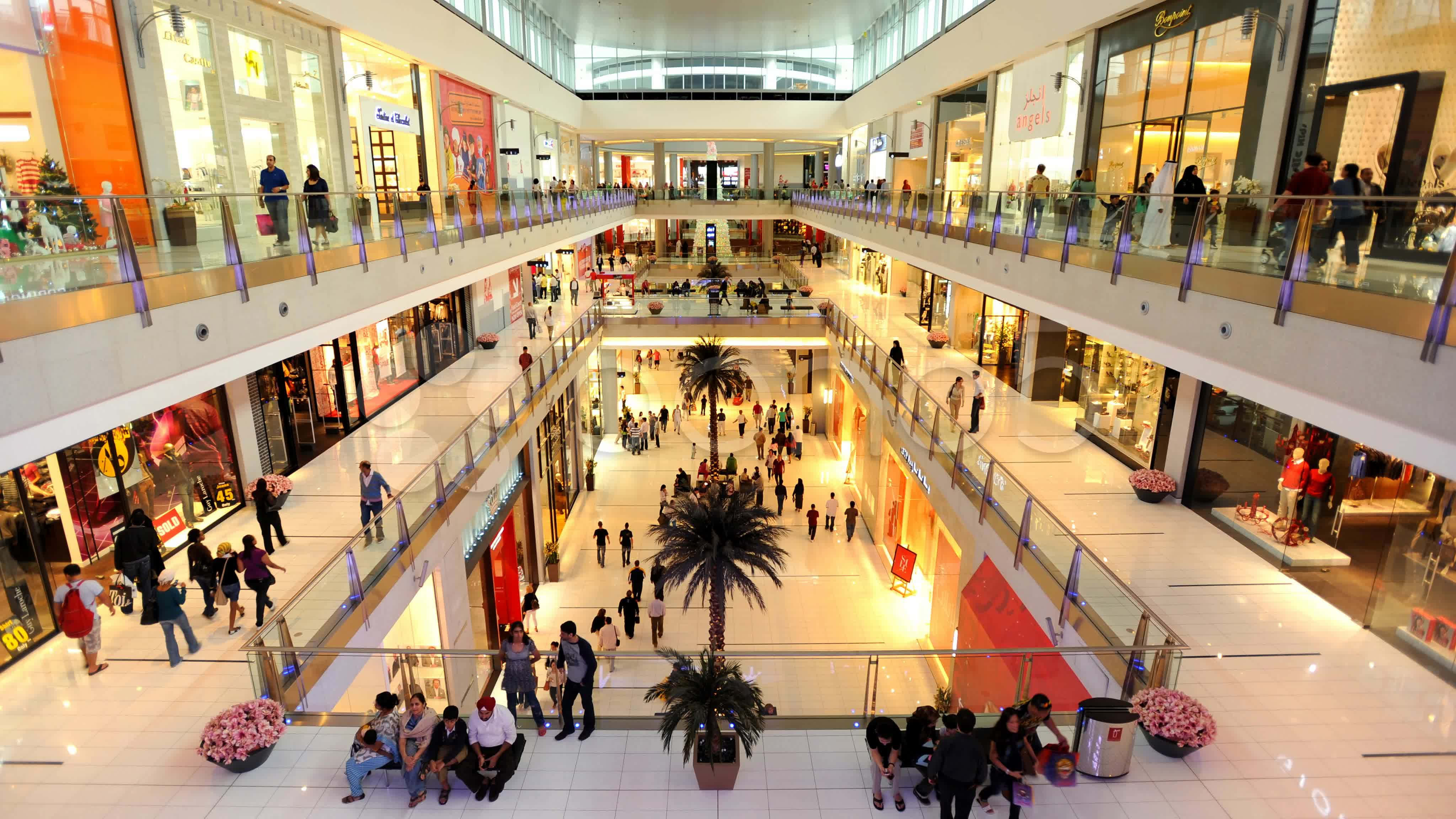 Shopping Mall 桌布 壁紙 — 一個繁忙的多層購物商場，購物者在中庭的商店和棕櫚樹之間穿梭。