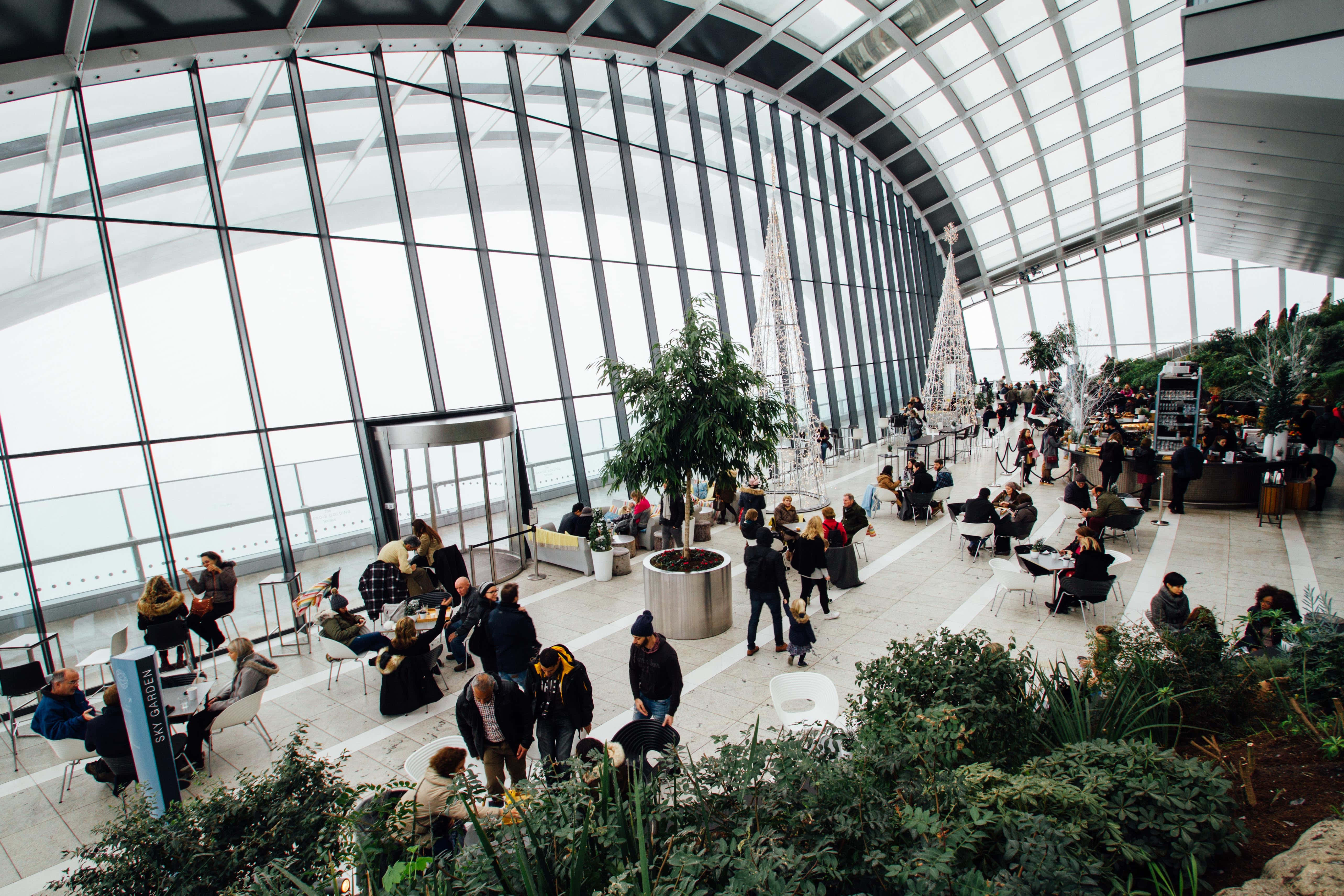 Airport 桌布 壁紙 — 一個繁忙的現代中庭，設有玻璃牆，人們在室內植物和節日樹木中放鬆身心。