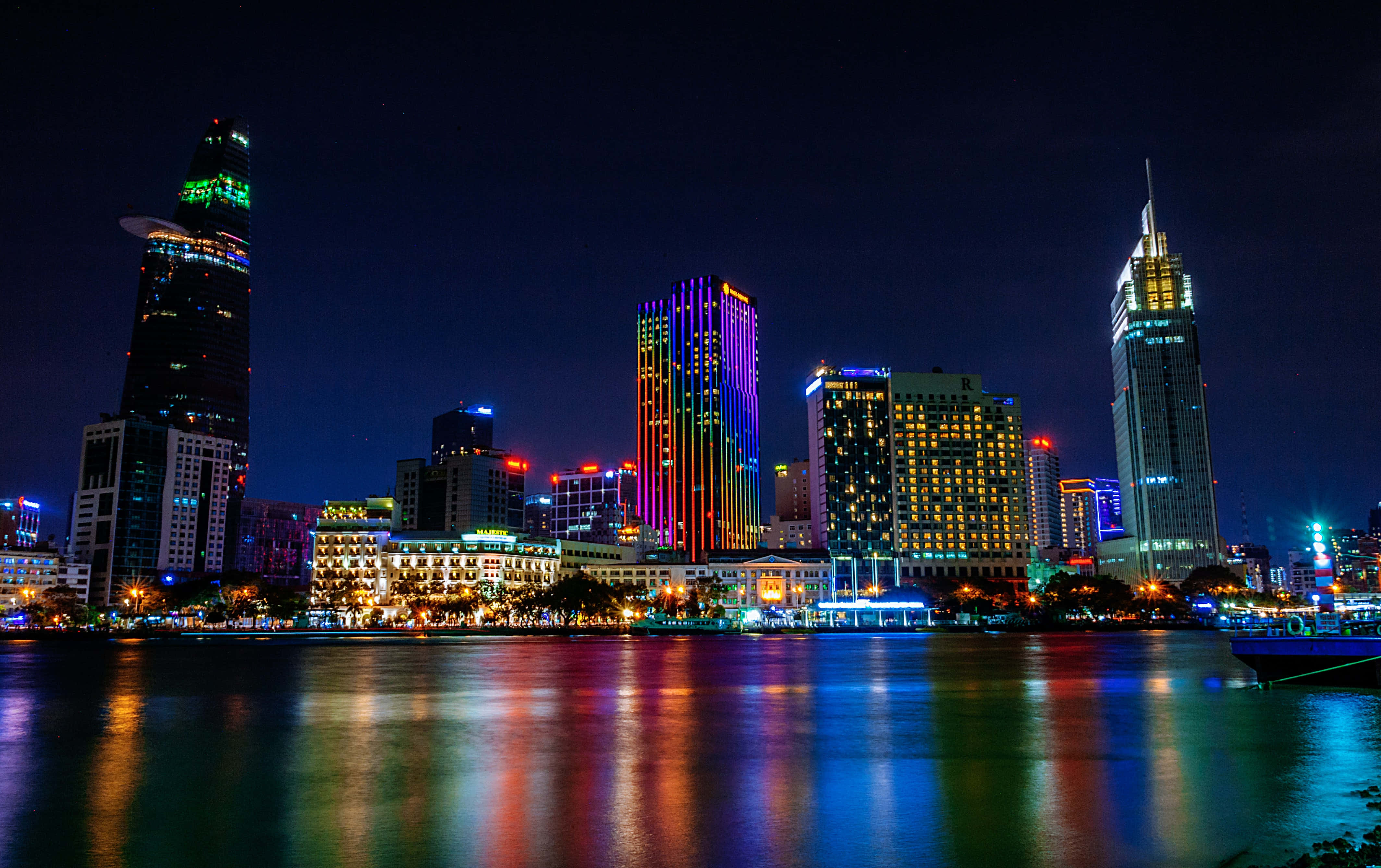 City Lights 桌布 壁紙 — 一個耀眼的夜景城市景觀，摩天大樓在霓虹色調中閃爍，倒映在平靜的河面上。