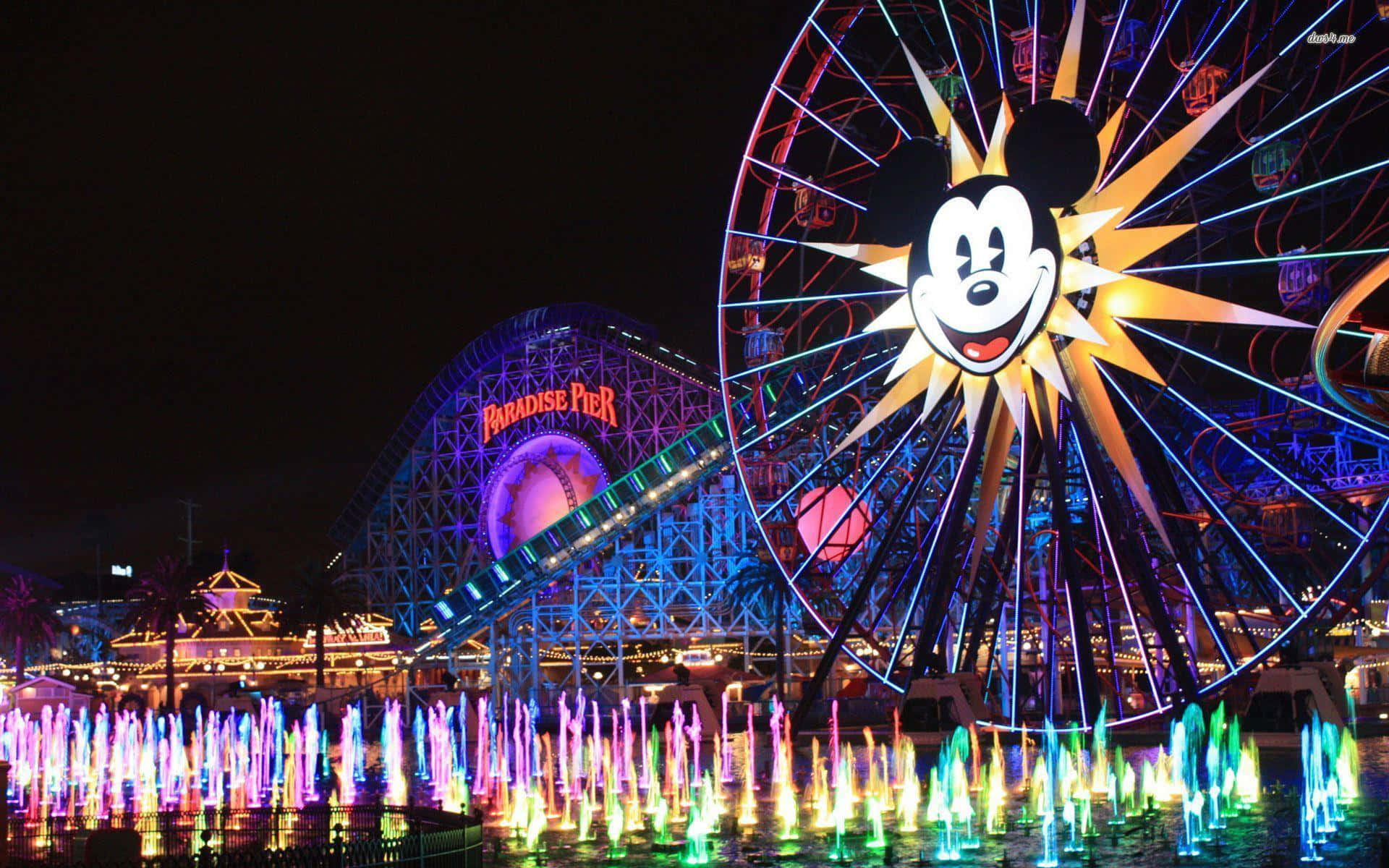 Disneyland 桌布 壁紙 — 一個耀眼的夜間遊樂場景，包含米奇老鼠摩天輪和色彩繽紛的噴泉，在漆黑的天空下。