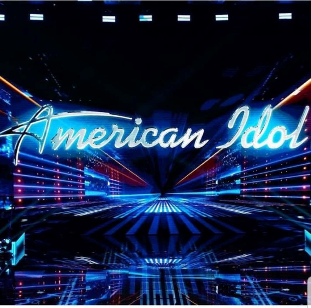 american idol 桌布 壁紙 — 一個耀眼的藍色「American Idol」霓虹標誌在充滿未來感的舞台上閃耀，配以激光燈光和反光地板。
