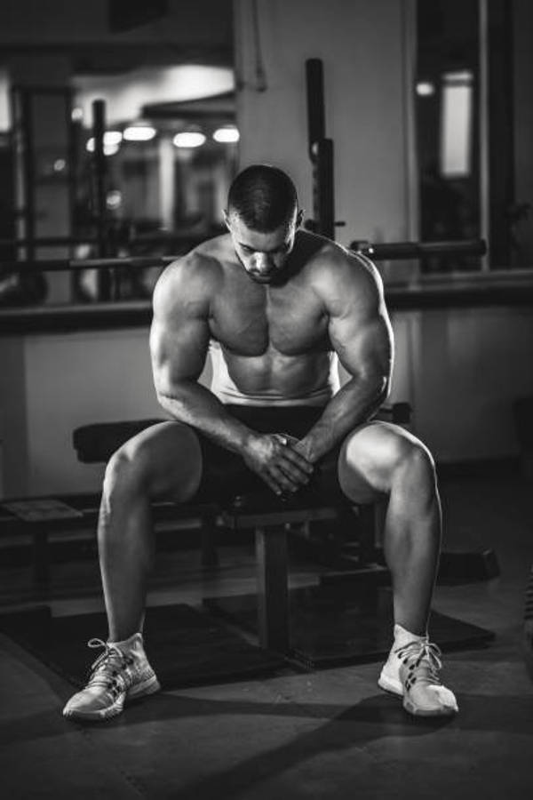 Exercise 桌布 壁紙 — 一個肌肉男坐在健身長椅上，低頭合十，周圍是舉重器材，黑白照片。