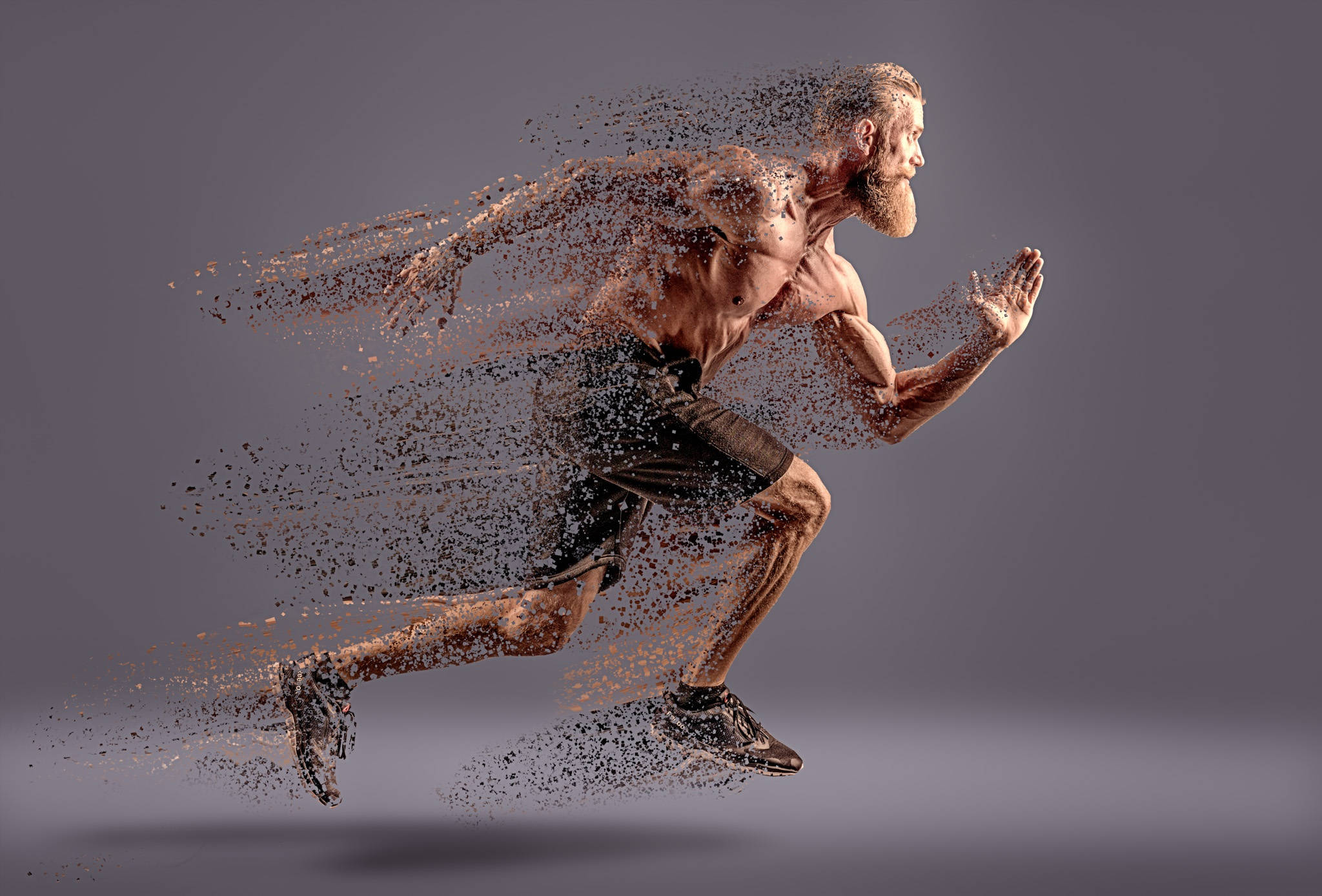 Running 桌布 壁紙 — 一個肌肉發達、留鬍子的男人向前衝刺，他的身體在灰色工作室背景前分解成粒子。