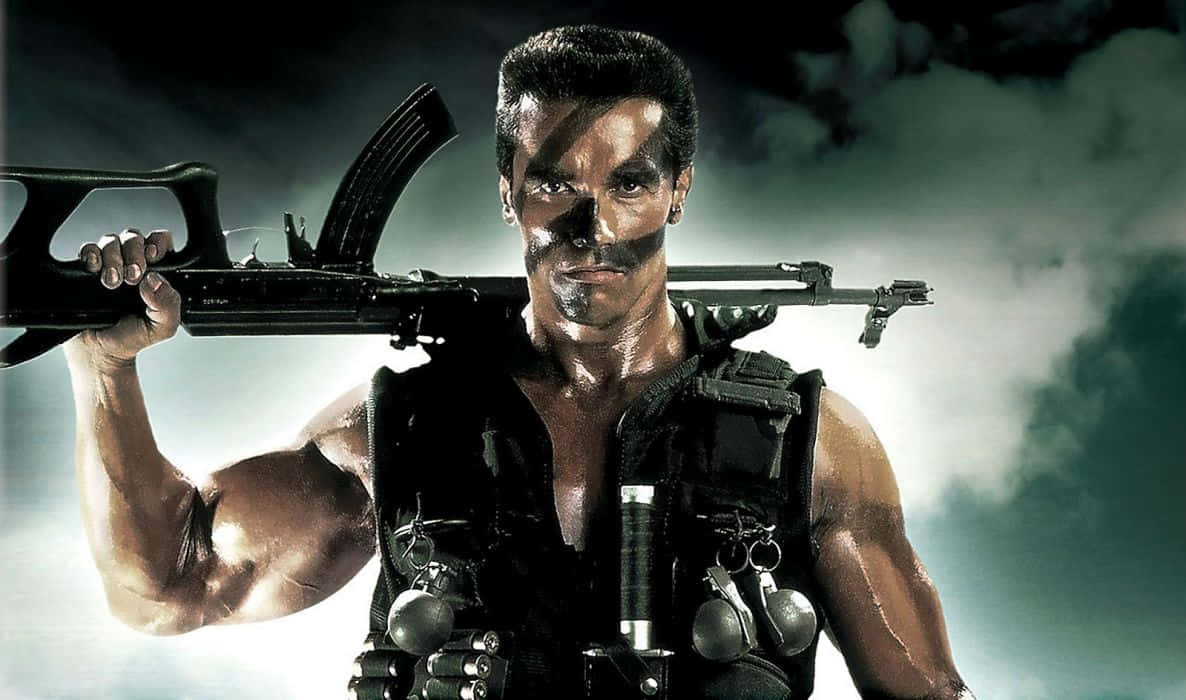 Action Movie 桌布 壁紙 — 一個肌肉發達、臉上塗有黑色顏料的男子，在暴風雨的天空下將突擊步槍扛在肩上。