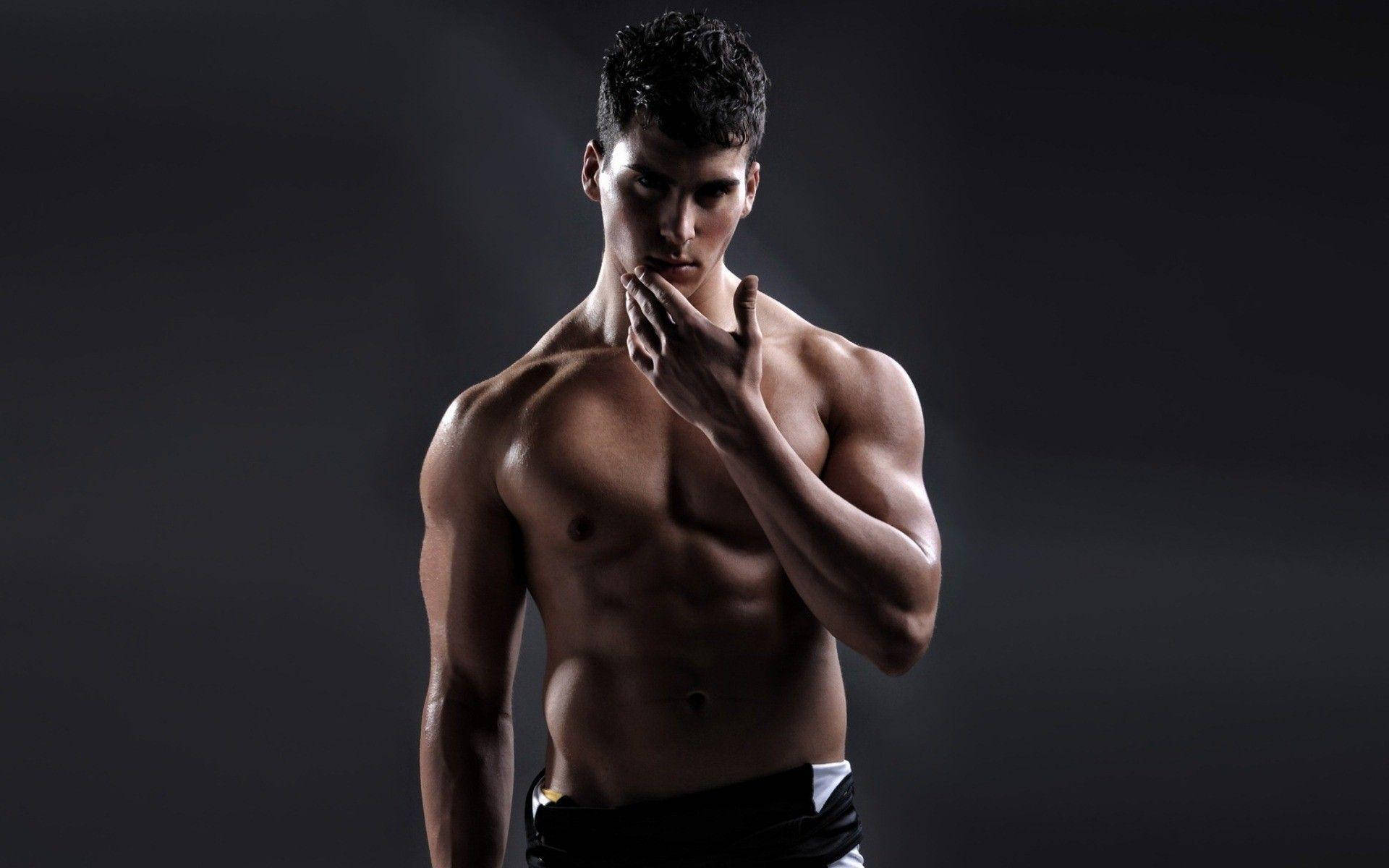 Handsome Shirtless Muscle Man 壁紙 — 一個肌肉發達、黑髮的男人赤膊站在黑色背景前，手靠近嘴巴，姿勢戲劇化。