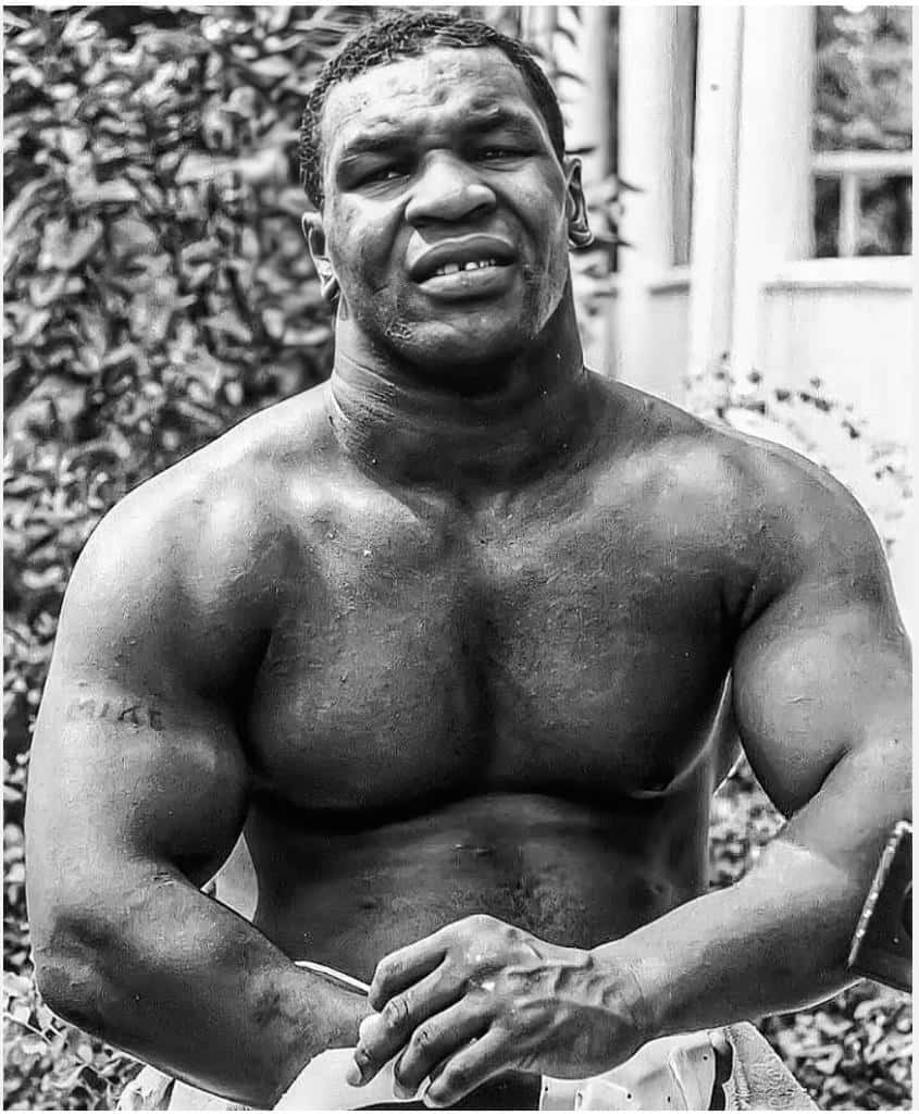 mike tyson 桌布 壁紙 — 一個肌肉發達嘅男人，手臂上有紋身，企喺戶外，背後有樹葉嘅黑白肖像。