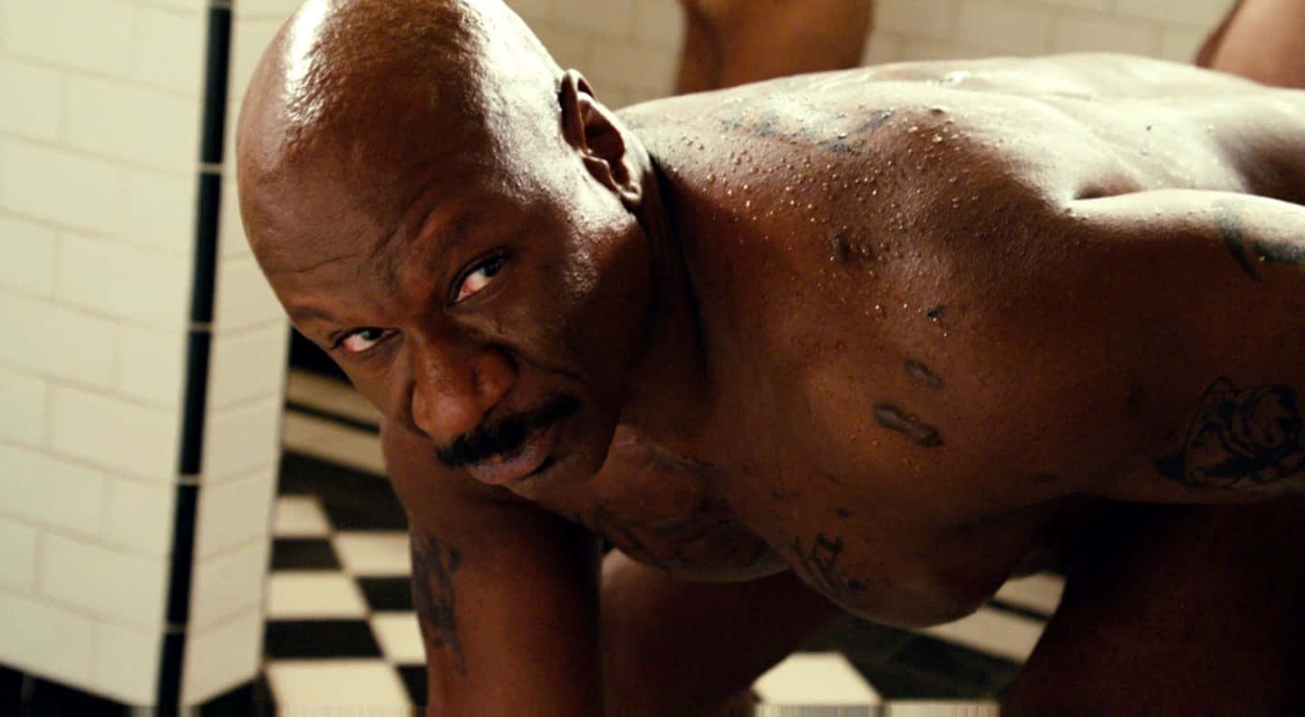 Ving Rhames 桌布 壁紙 — 一個肌肉發達的光頭紋身男子在瓷磚浴室中向前傾，汗水在皮膚上閃閃發光，他專注地凝視著相機。
