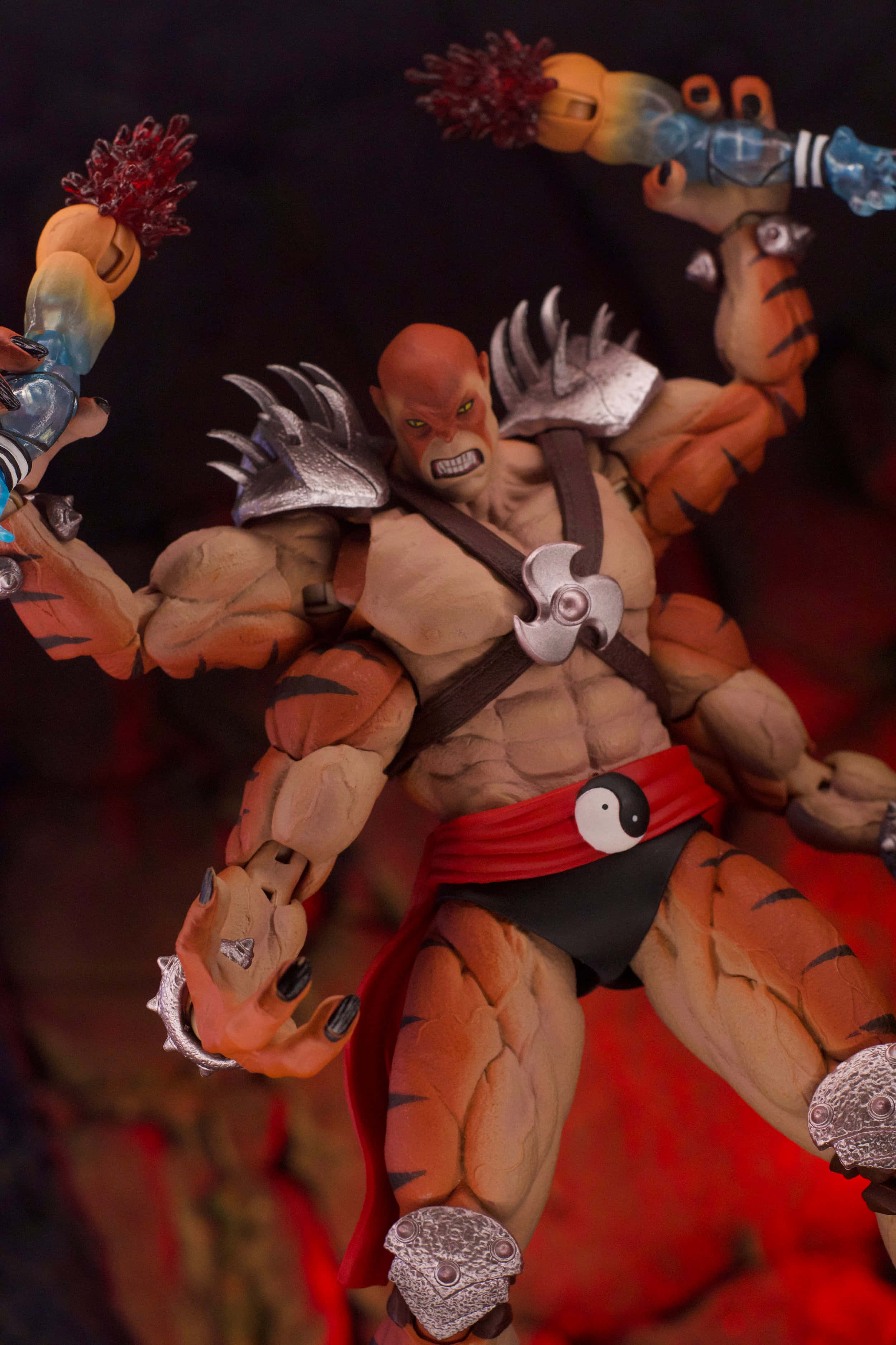 Mortal Kombat Kintaro 桌布 壁紙 — 一個肌肉發達的動作人偶，擁有老虎條紋皮膚和銀色盔甲，在火紅背景前揮舞帶刺武器。