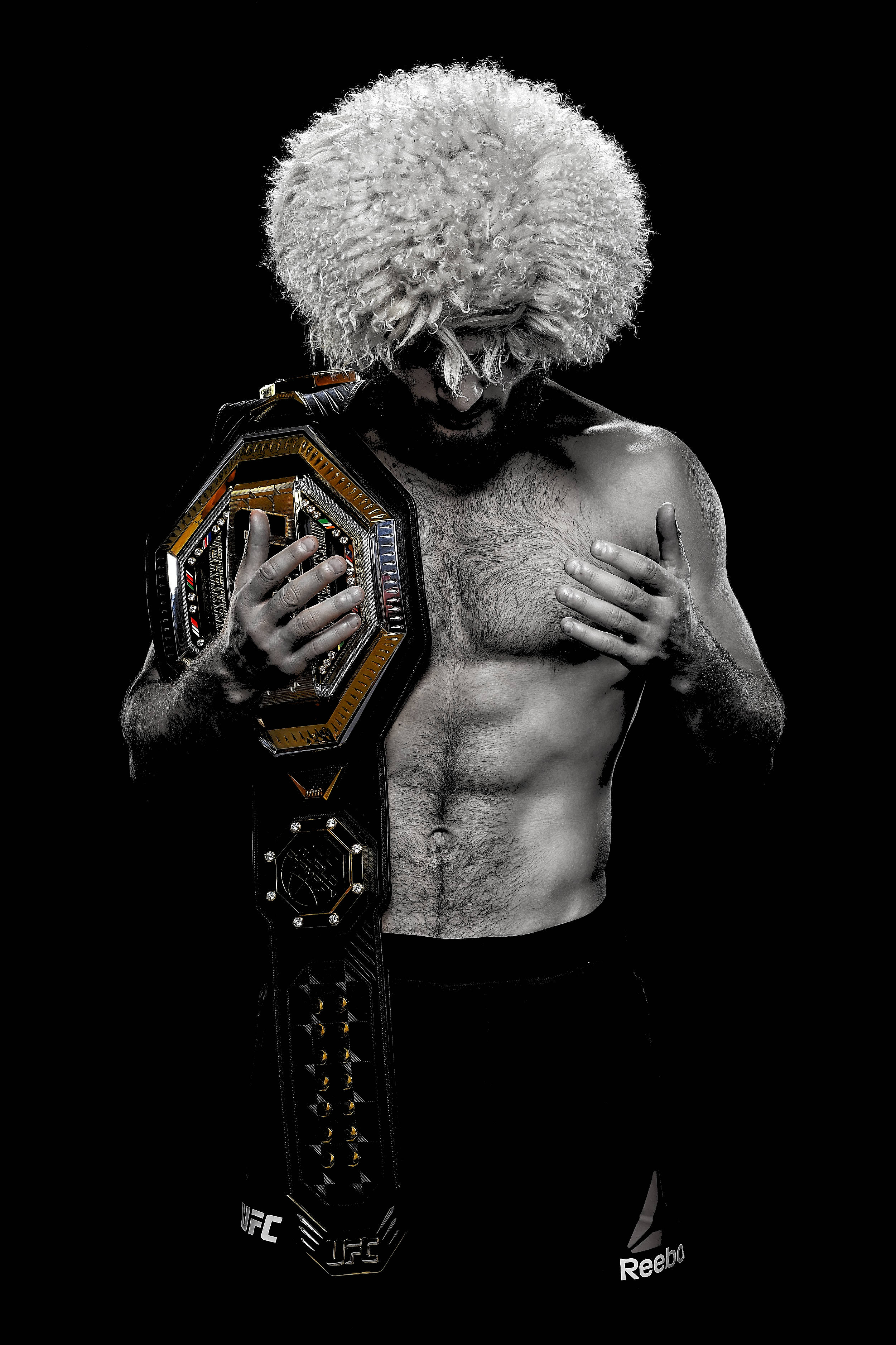 UFC 桌布 壁紙 — 一個肌肉發達的戰士戴著蓬鬆的白色假髮，在純黑背景前高舉UFC冠軍腰帶。