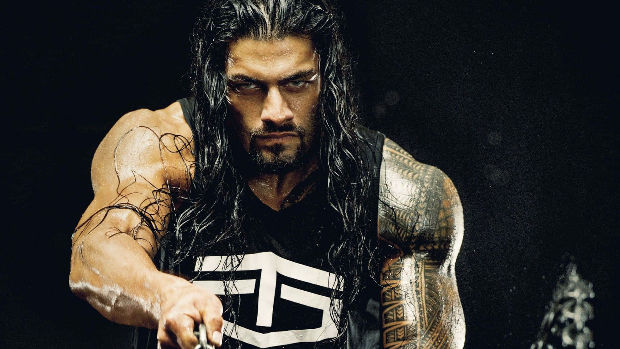 Roman Reigns 桌布 壁紙 — 一個肌肉發達的摔角手，長濕頭髮和紋身，在黑暗背景下拿著鏈條，眼神專注。