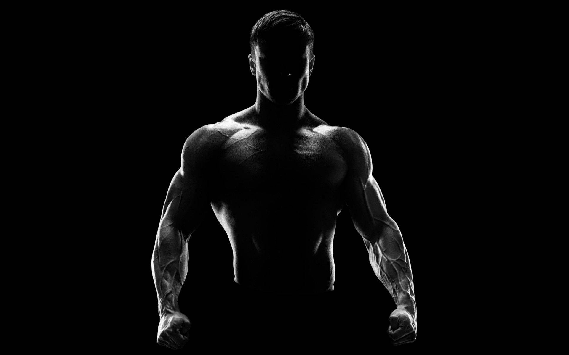 Muscle Man Silhouette In Fighter Stance 壁紙 — 一個肌肉發達的男人以剪影站在黑色背景前，戲劇性的燈光突顯他清晰的體格。