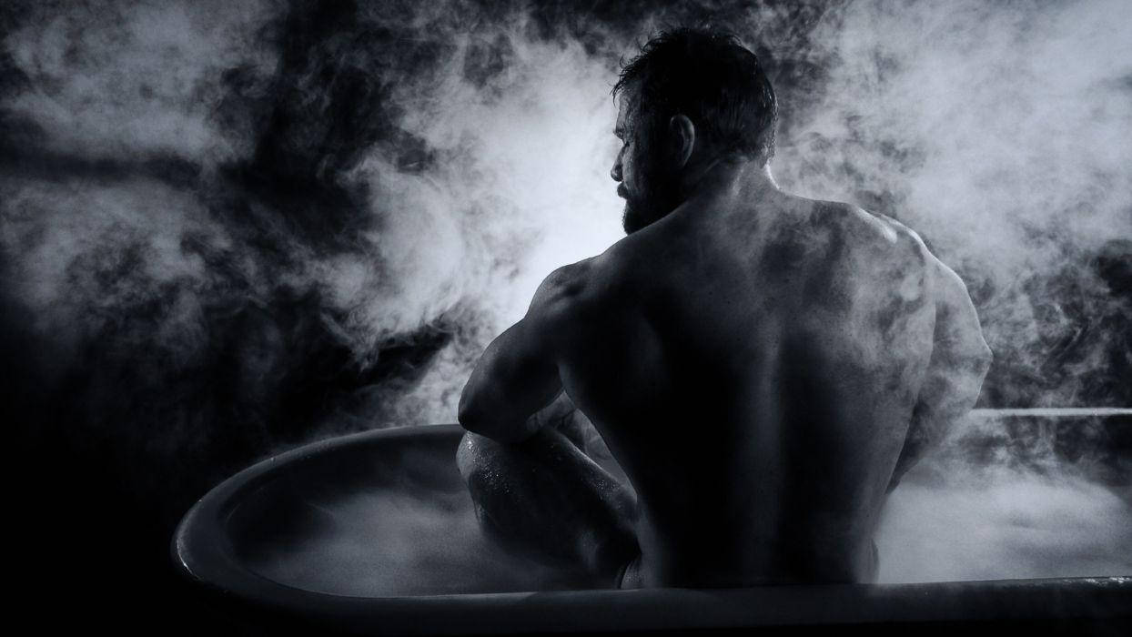 Robust Physique: The Epitome of Raw Power and Strength 壁紙 — 一個肌肉發達的男人坐在冒著蒸汽的浴缸中，被旋轉的霧氣包圍，在戲劇性的黑白燈光下。