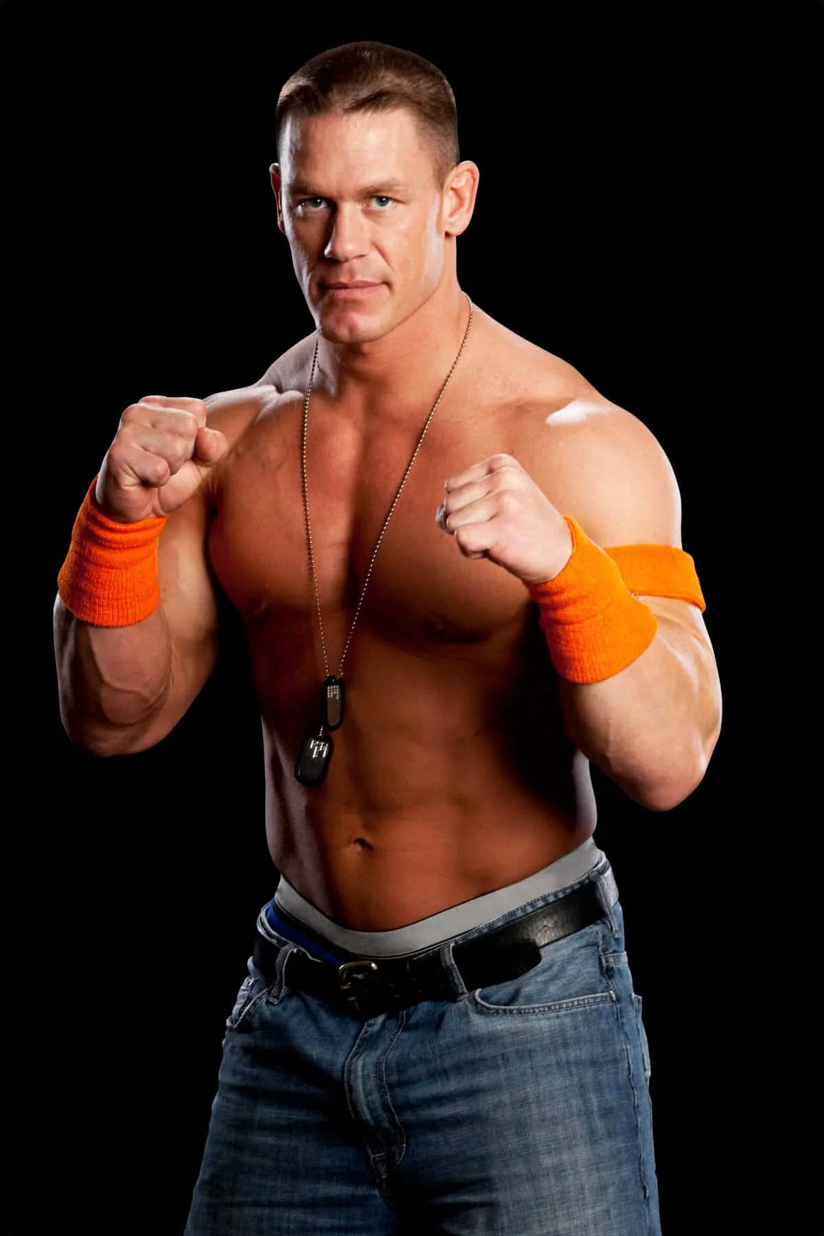 John Cena 桌布 壁紙 — 一個肌肉發達的男人戴著橙色腕帶和牛仔褲，在黑色背景前握緊拳頭擺姿勢。