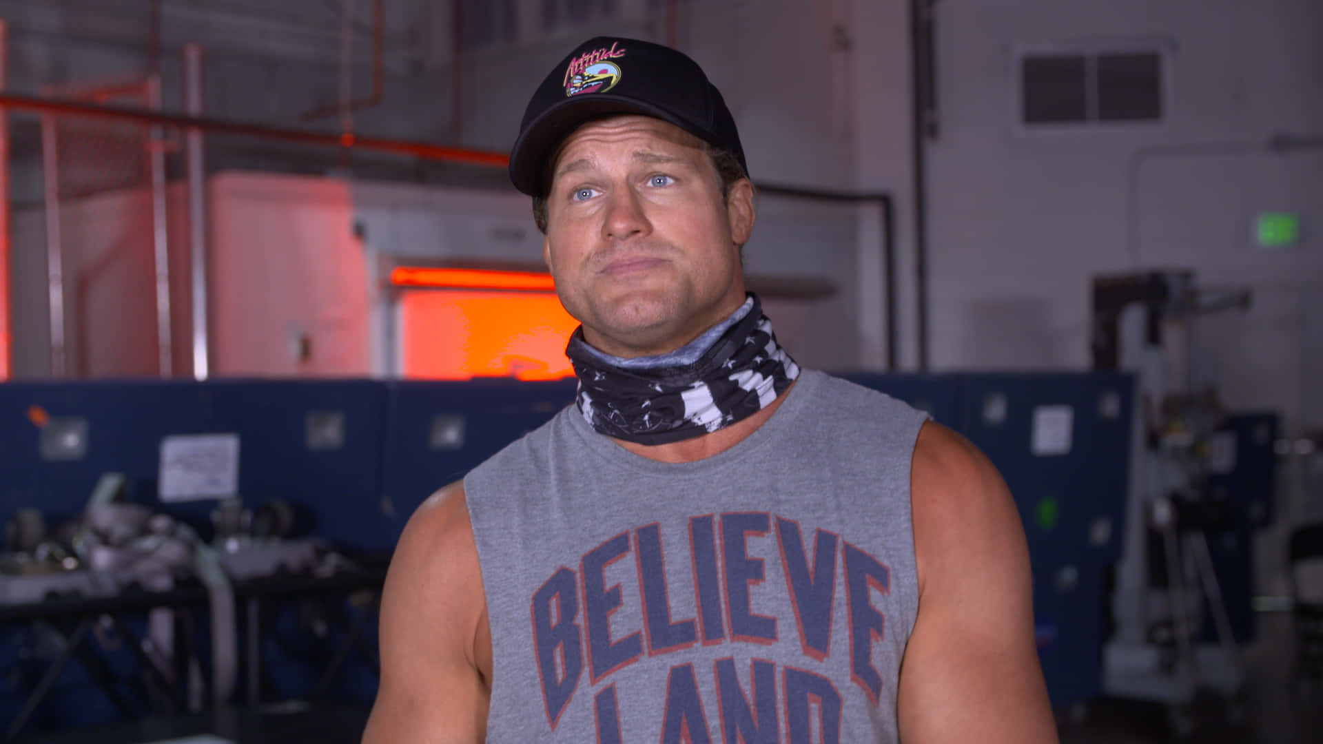 Dolph Ziggler Casual Attire 壁紙 — 一個肌肉發達的男人穿著灰色背心和黑色帽子，站在光線昏暗、背景有紅色燈光的健身房裡。