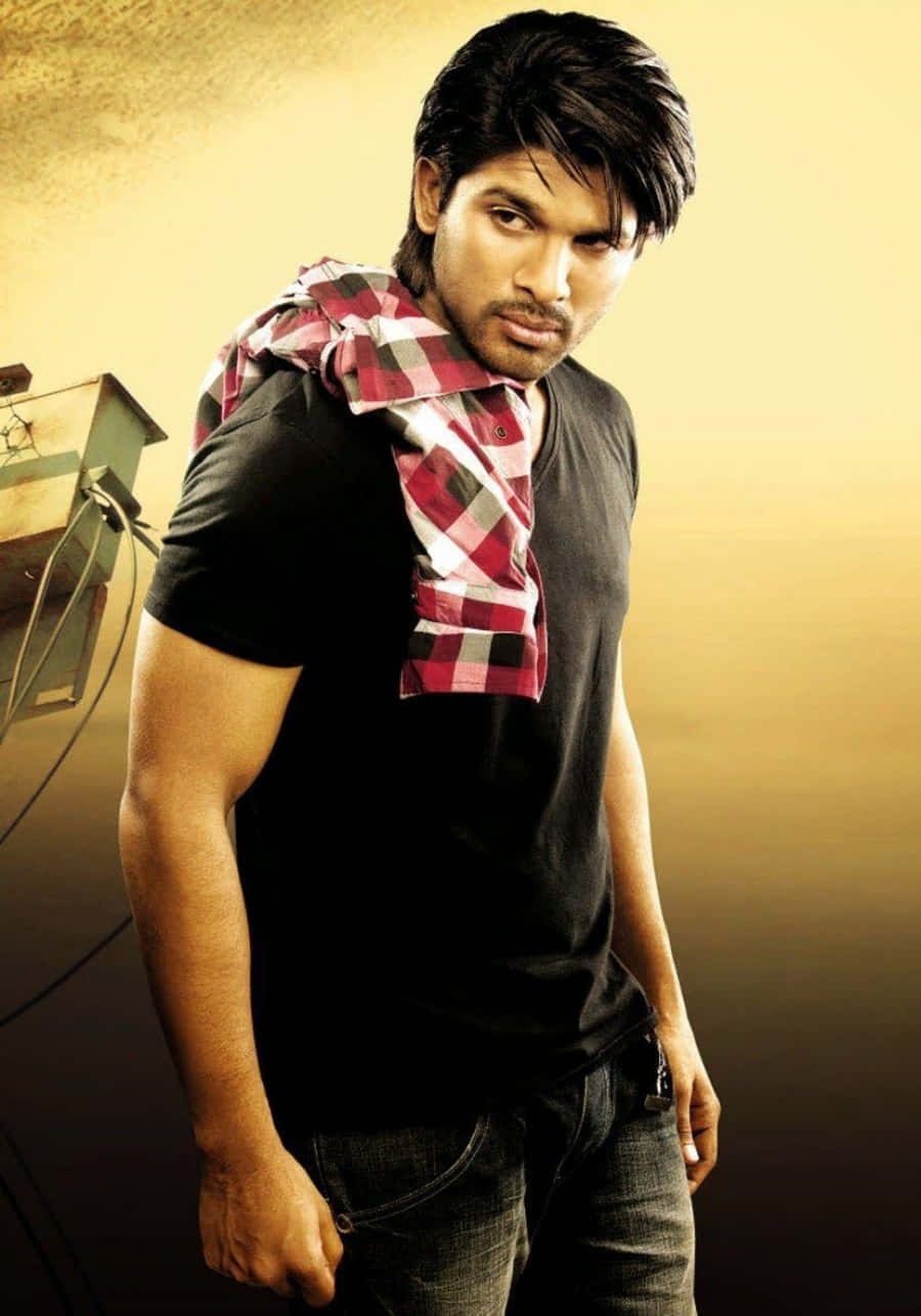 Allu Arjun 桌布 壁紙 — 一個肌肉發達的男人穿著黑色T恤和牛仔褲，肩上披著一條紅色格仔圍巾，在溫暖的金色漸變背景前自信地擺姿勢。
