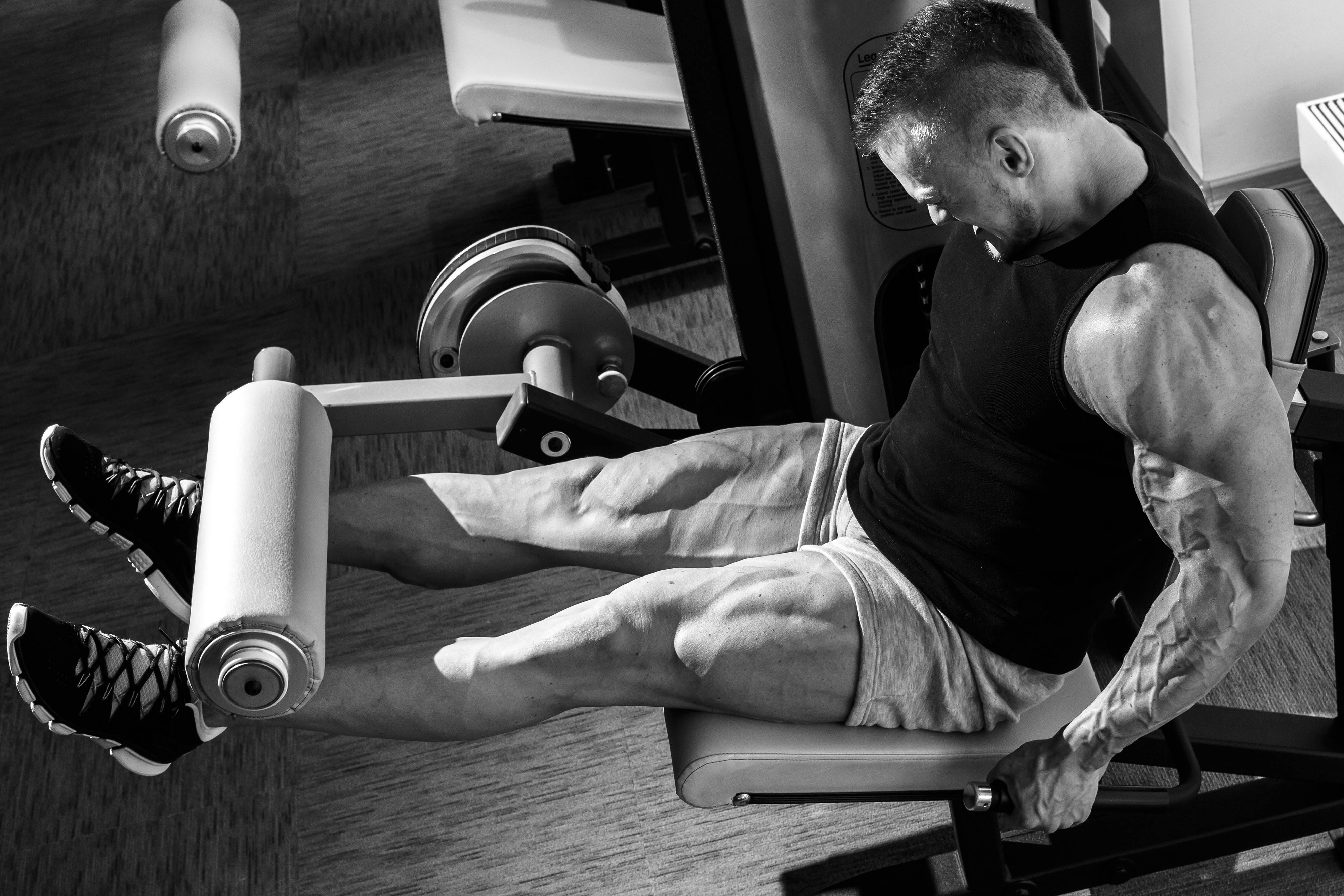 Exercise 桌布 壁紙 — 一個肌肉發達的男子在健身室中於腿部推舉機上劇烈鍛煉，以高對比度黑白捕捉。