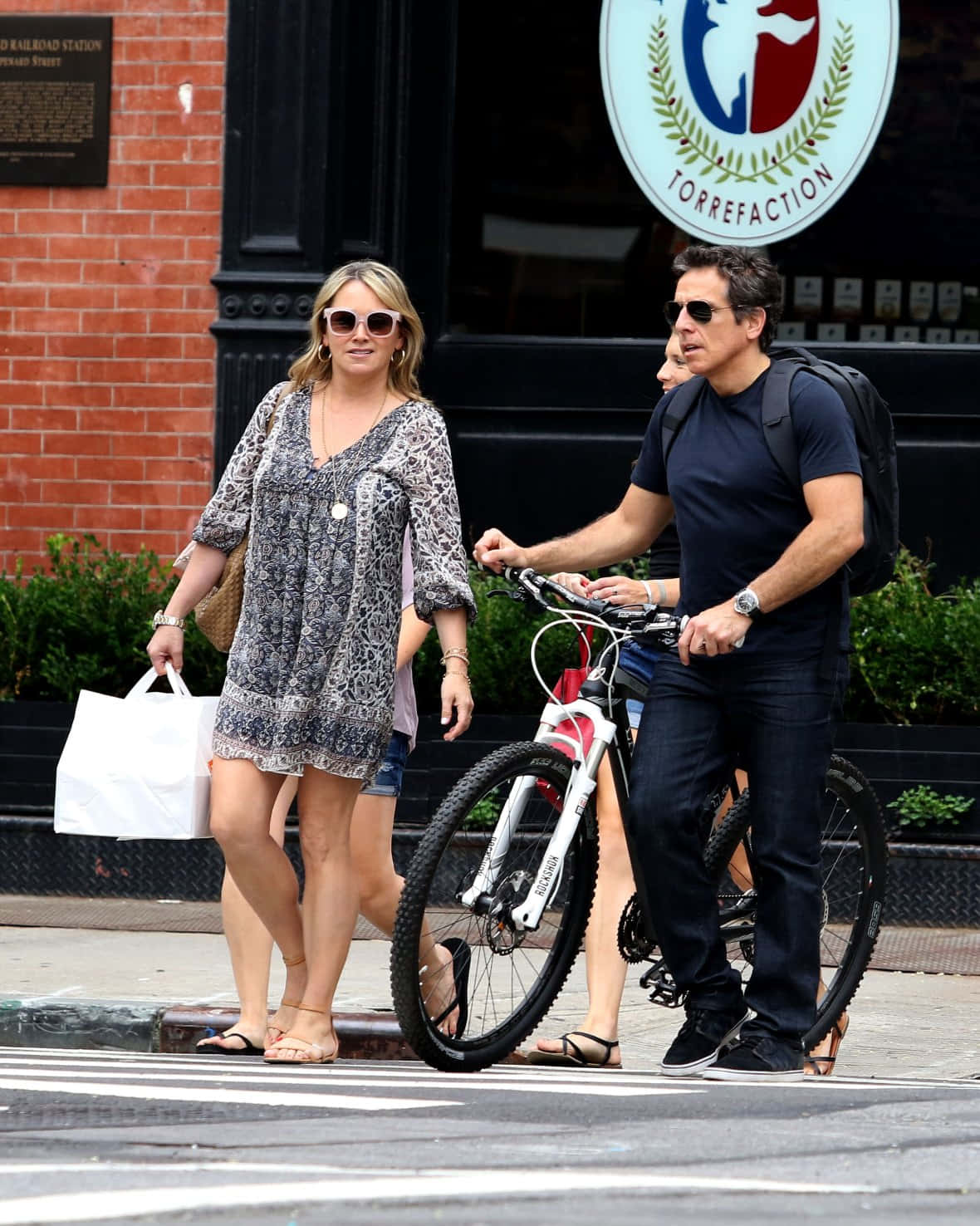 Christine Taylor 桌布 壁紙 — 一個背著背包的男人推著單車，旁邊一個女人拿著白色購物袋，在城市的行人路上行走。