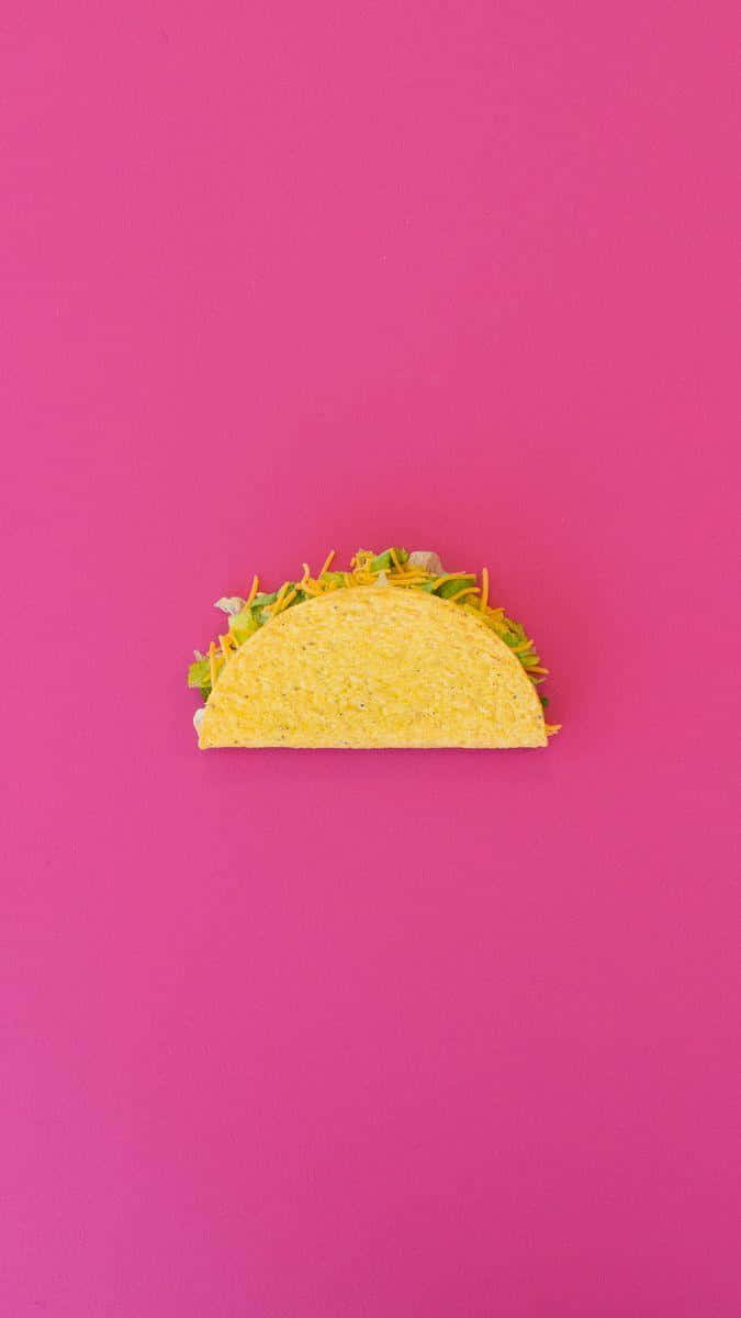 Taco 桌布 壁紙 — 一個脆皮墨西哥卷餅，上面有切碎的芝士和生菜，置於鮮豔的粉紅色背景中央。