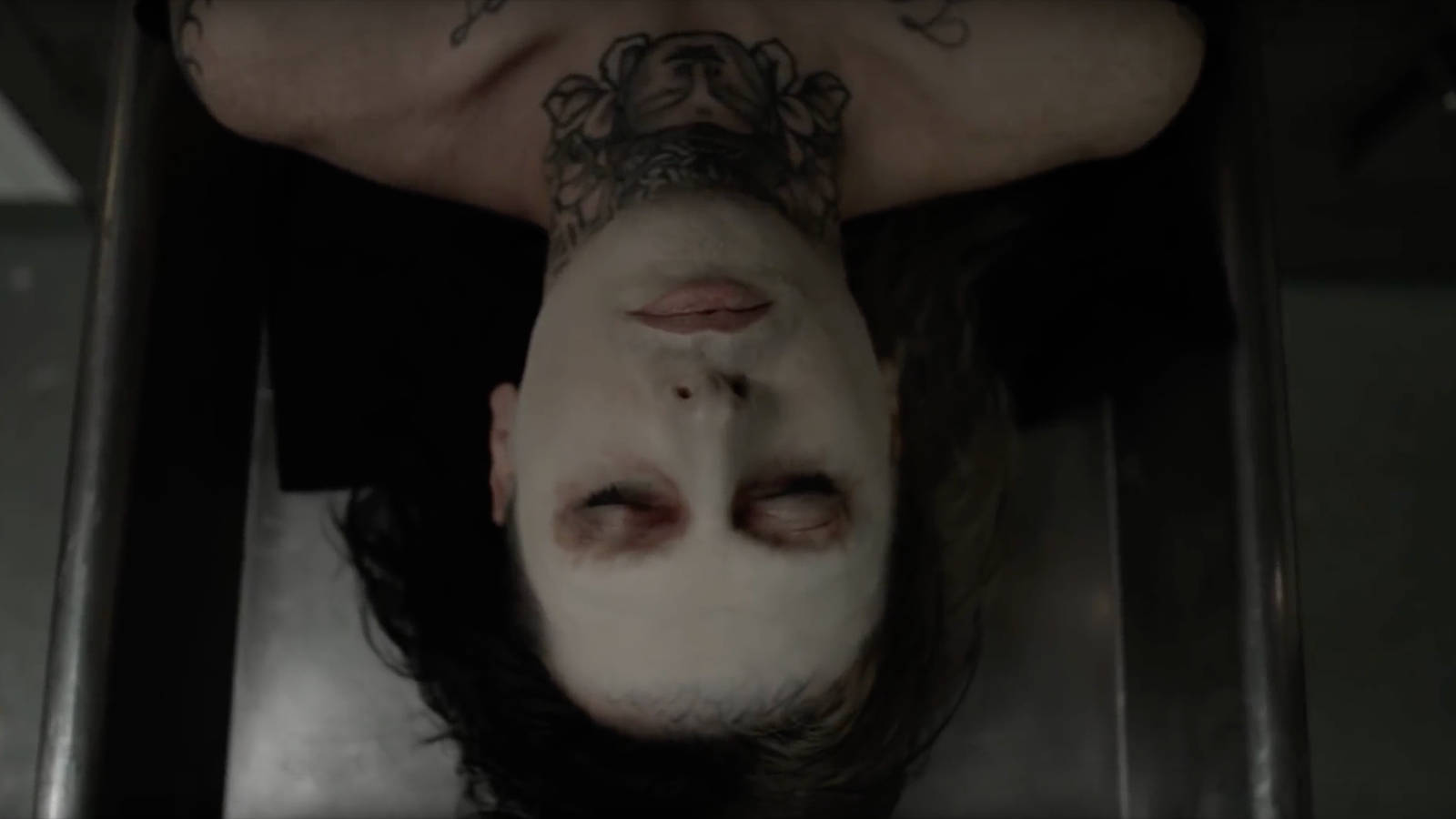 Ghostemane 桌布 壁紙 — 一個臉上塗有白色顏料、頸部有紋身的人，倒掛在一個金屬棺材狀的結構中。