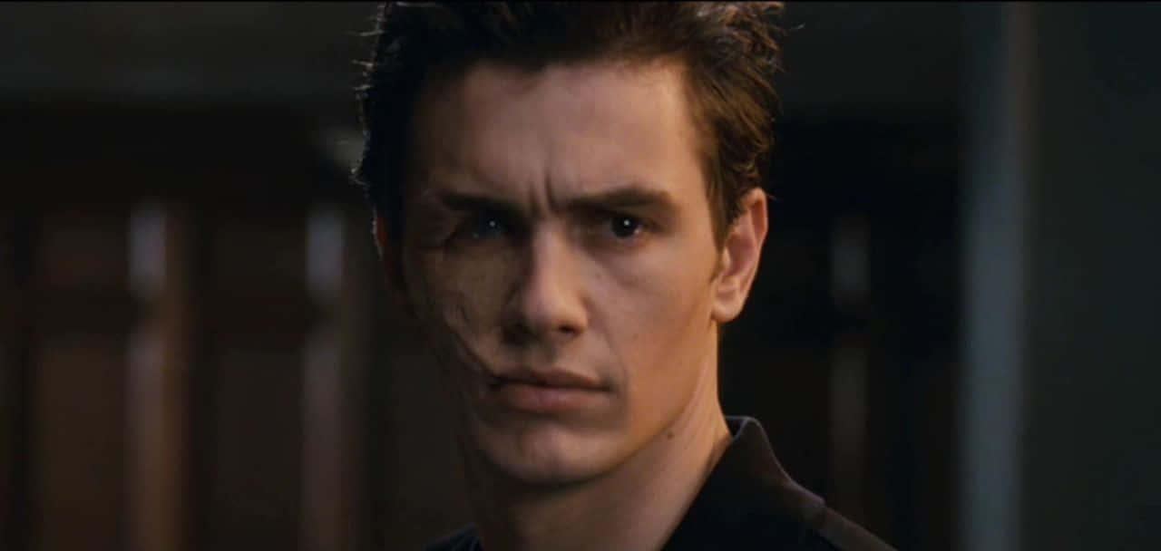 Harry Osborn 桌布 壁紙 — 一個臉頰有疤痕的男人特寫，在昏暗的室內環境中強烈凝視。