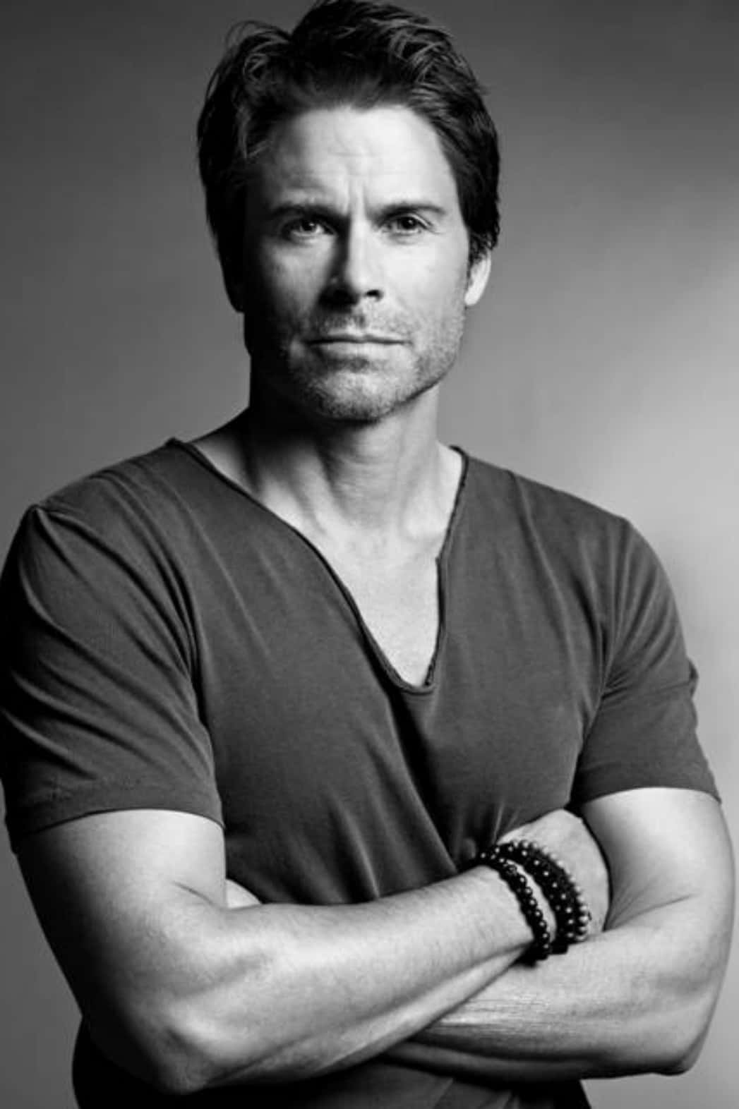 rob lowe 桌布 壁紙 — 一個自信的男人交叉雙臂，在清晰的黑白工作室肖像中直視鏡頭。