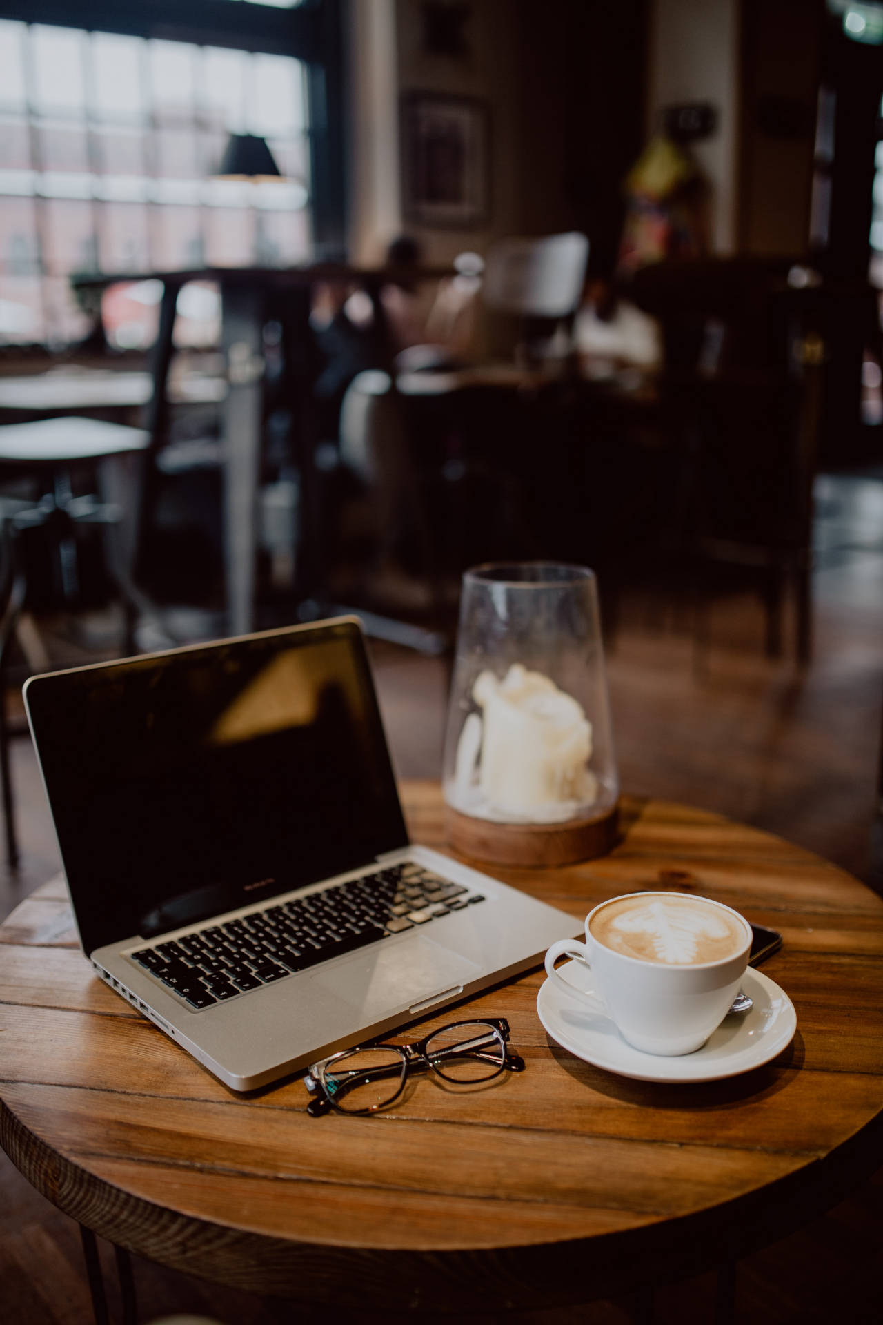 Best Laptop 桌布 壁紙 — 一個舒適的咖啡廳場景，筆記型電腦、咖啡杯和眼鏡放在木桌上，沐浴在溫暖的自然光中。