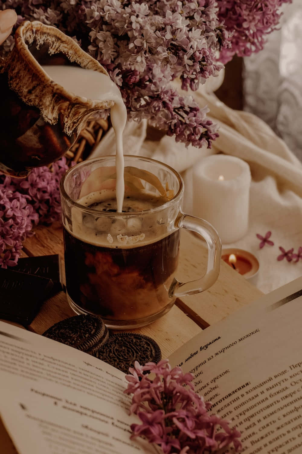 Floral Tea 桌布 壁紙 — 一個舒適的場景，牛奶倒入咖啡中，旁邊有丁香、朱古力曲奇和點燃的蠟燭在木桌上。