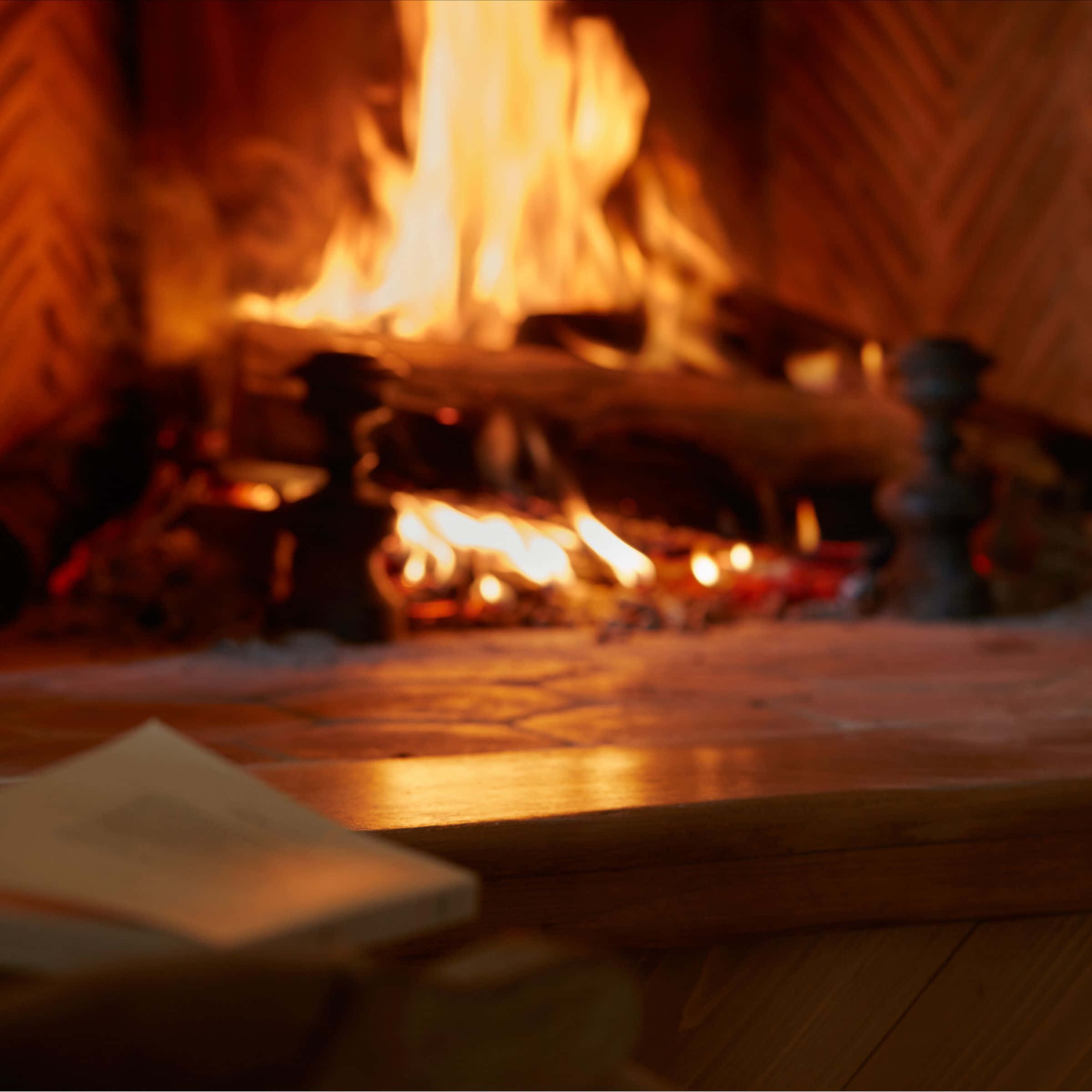 Cozy Fire 桌布 壁紙 — 一個舒適的壁爐，噼啪作響的火焰在木製壁爐架和地板上投射出溫暖的金色光芒。