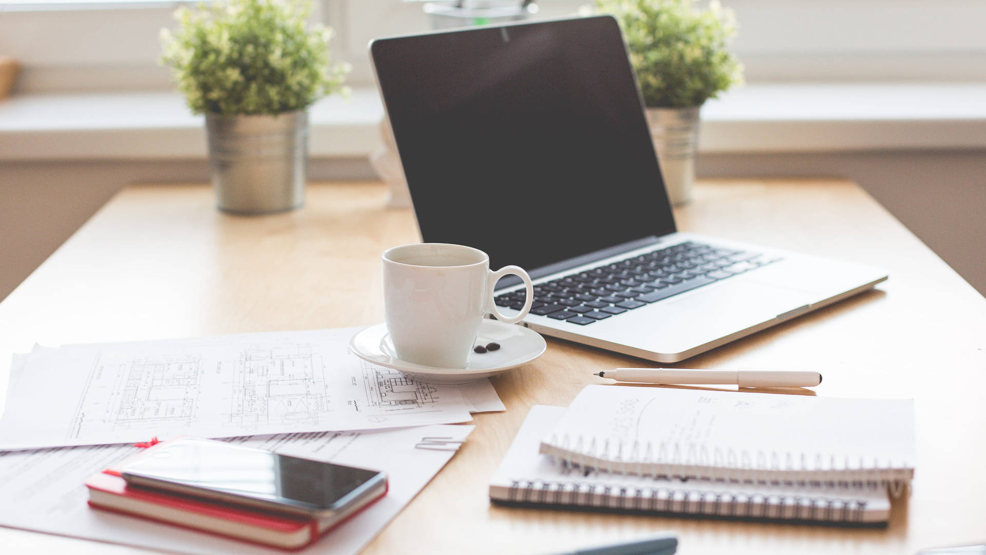 Working From Home 桌布 壁紙 — 一個舒適的家庭辦公室書桌，配有手提電腦、咖啡杯、筆記本和盆栽植物，沐浴在柔和自然光中。