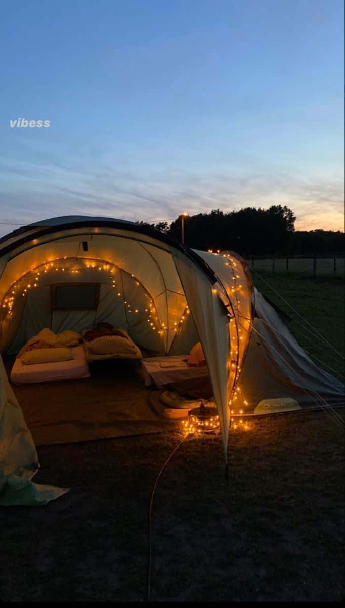 Winter Camping 桌布 壁紙 — 一個舒適的帳篷在黃昏時分用串燈溫暖地發光，露出裡面草地上舒適的床鋪。
