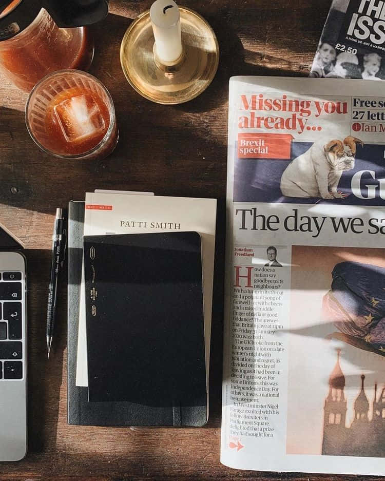 溫習 桌布 壁紙 — 一個舒適的書桌場景，有報紙Brexit特刊、雞尾酒、蠟燭、筆記本和手提電腦，沐浴在溫暖的陽光中。