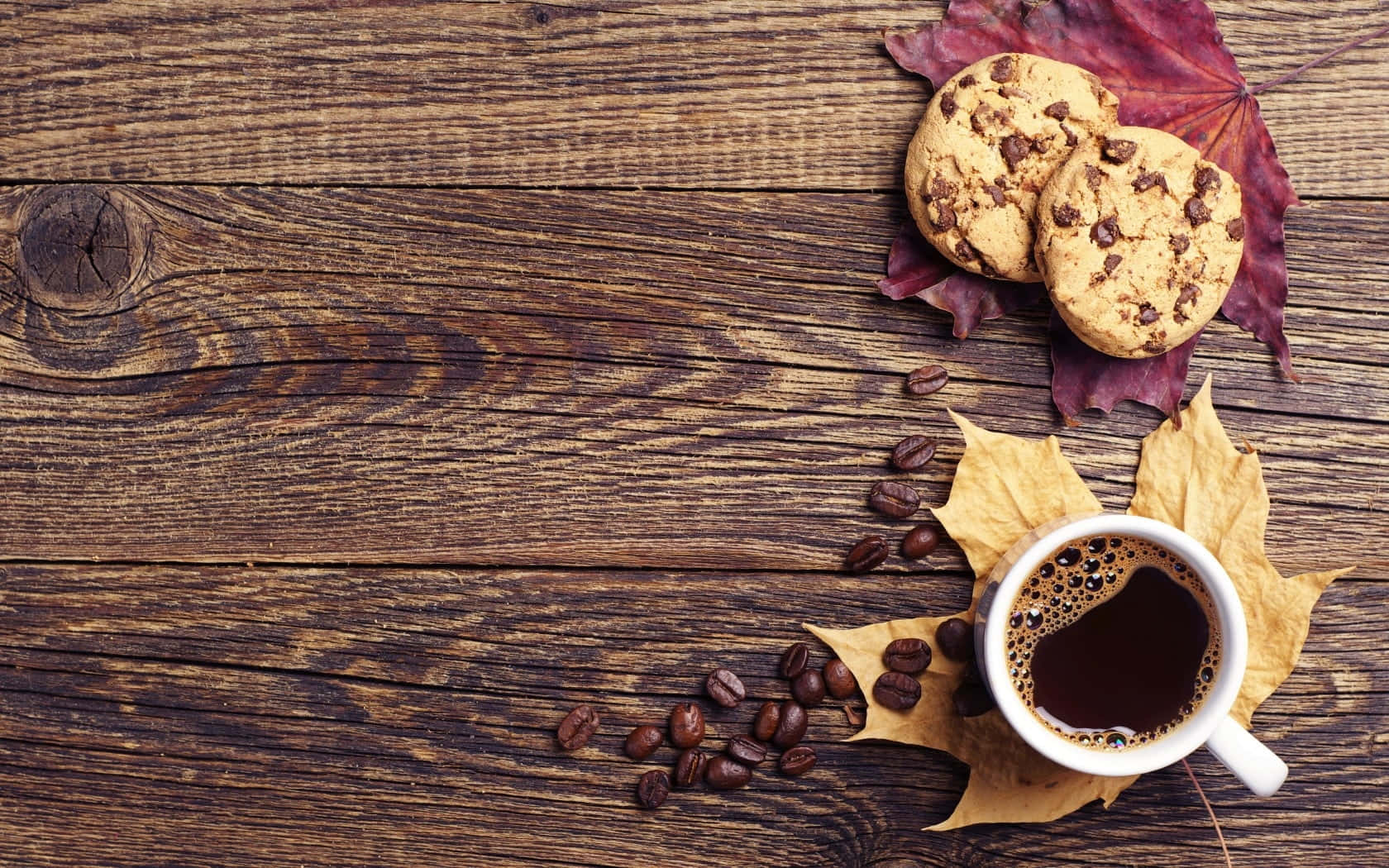 Autumn Food 桌布 壁紙 — 一個舒適的秋日場景，一杯冒著熱氣的咖啡、朱古力曲奇和散落的咖啡豆，放在裝飾著鮮豔秋葉的質樸木板上。
