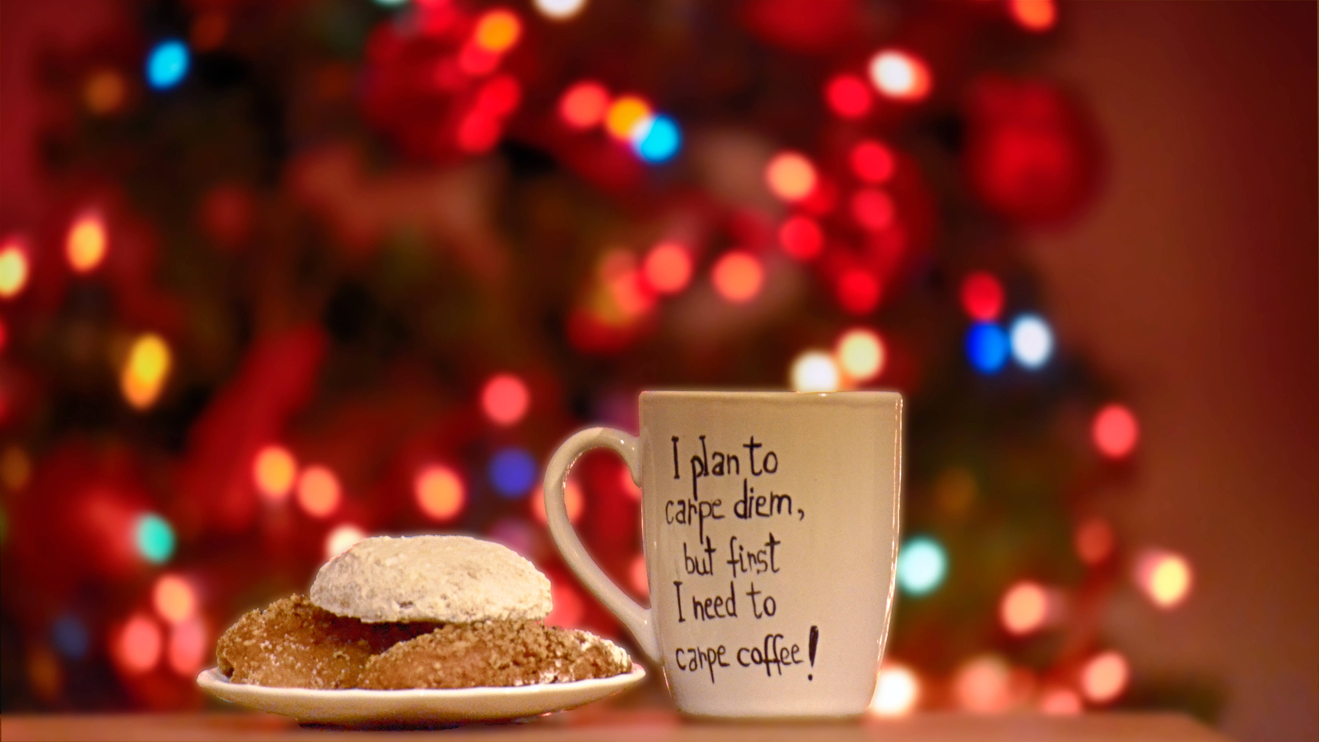 Santa Claus 桌布 壁紙 — 一個舒適的馬克杯，上面寫著「I plan to carpe diem but first I need to carpe coffee」，旁邊放著撒了糖的餅乾，背景是節日氣氛的散景聖誕樹。