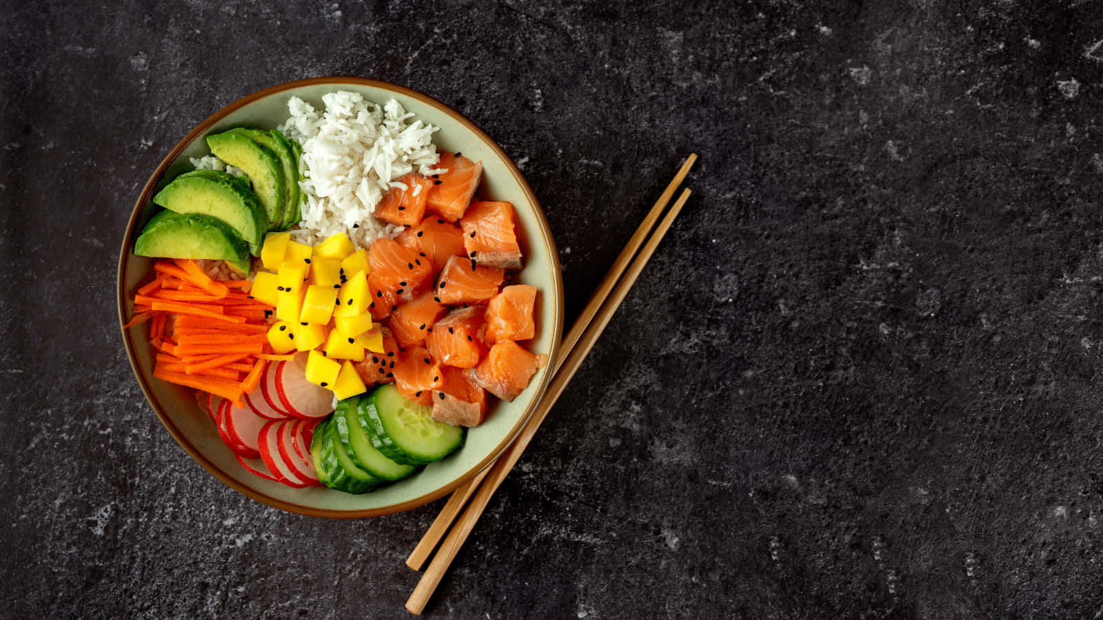 Sushi 桌布 壁紙 — 一個色彩繽紛的 poke bowl，上面有三文魚、芒果、牛油果和米飯，放在深色石面上，旁邊有筷子。