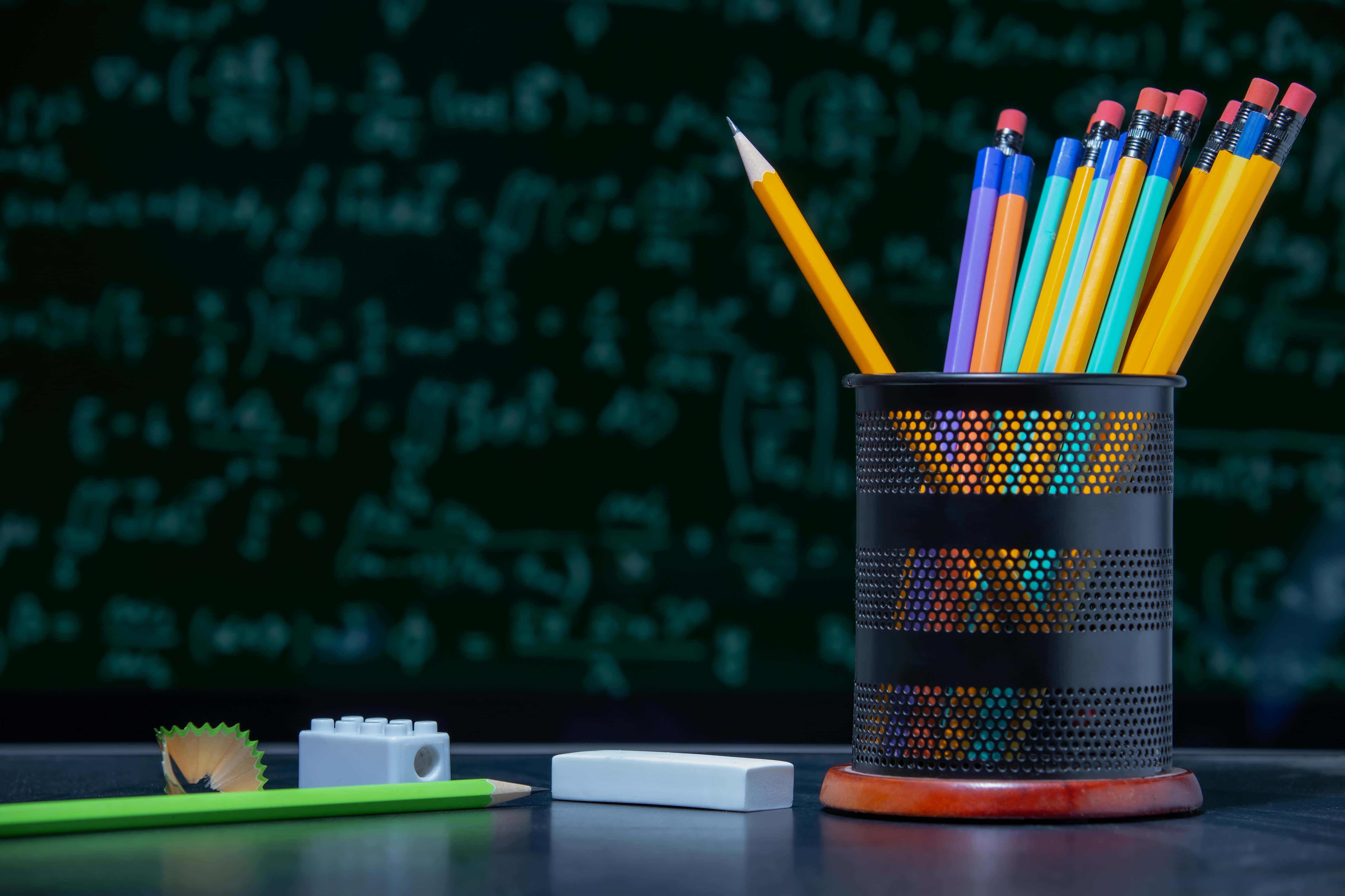 Back To School 桌布 壁紙 — 一個色彩繽紛的筆筒裝滿了削尖的鉛筆，放在一張桌子上，前面是一塊佈滿數學方程式的黑板。