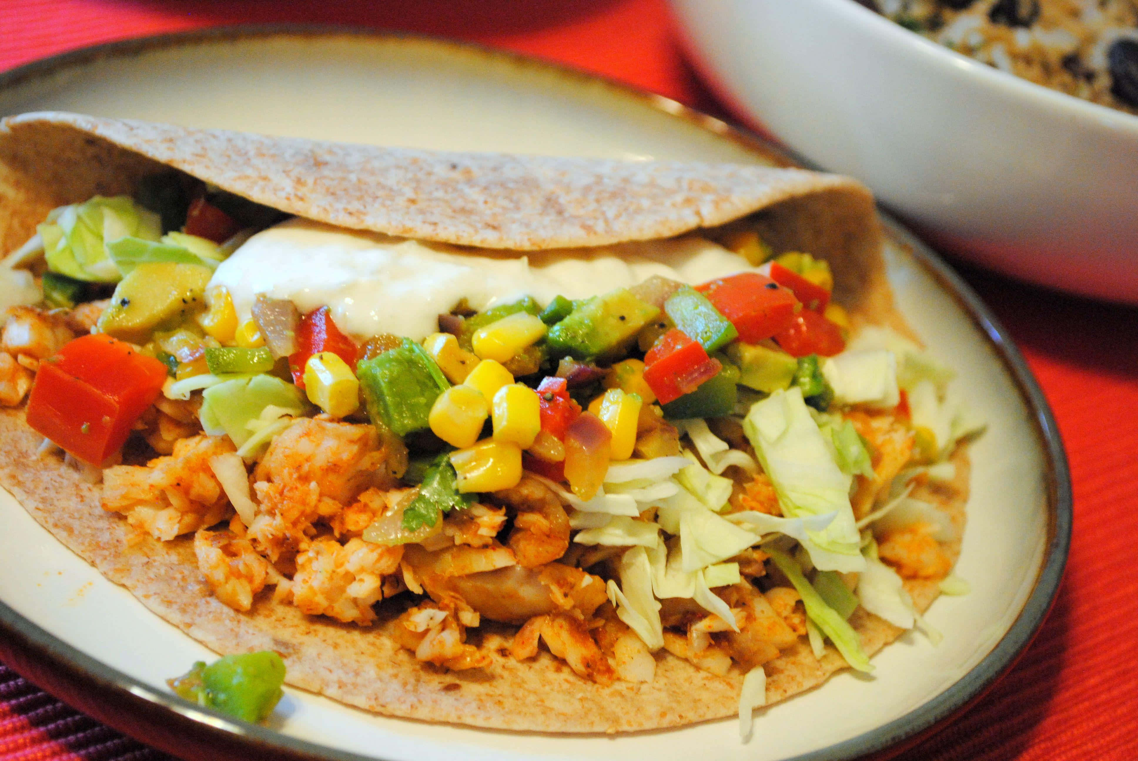 Taco 桌布 壁紙 — 一個色彩繽紛的雞肉墨西哥卷特寫，上面放有粟米、牛油果和酸忌廉，盛載在碟上。